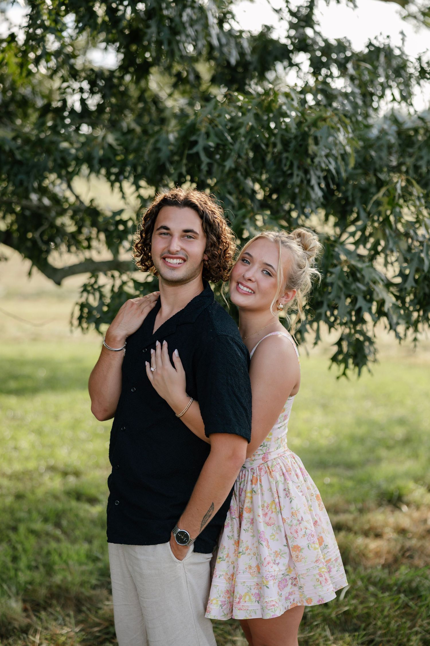 A couple embraces under tree branches in a romantic outdoor photoshoot.