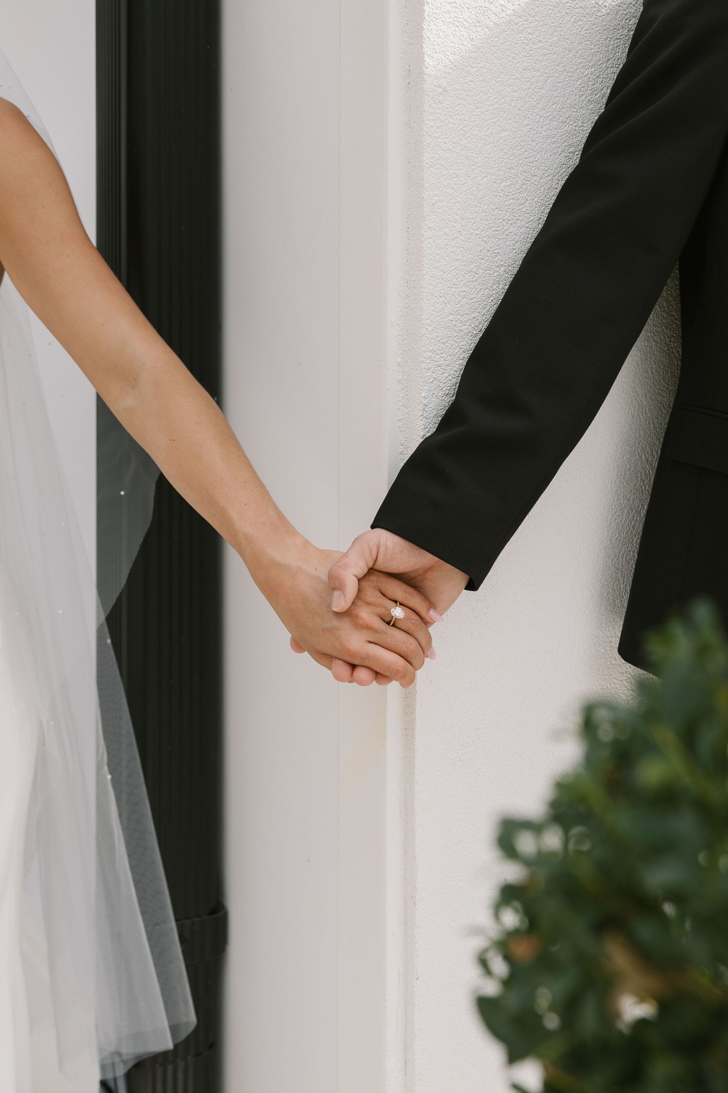 Close-up view of newlywed couple holding hands with white wedding dress and black suit visible.