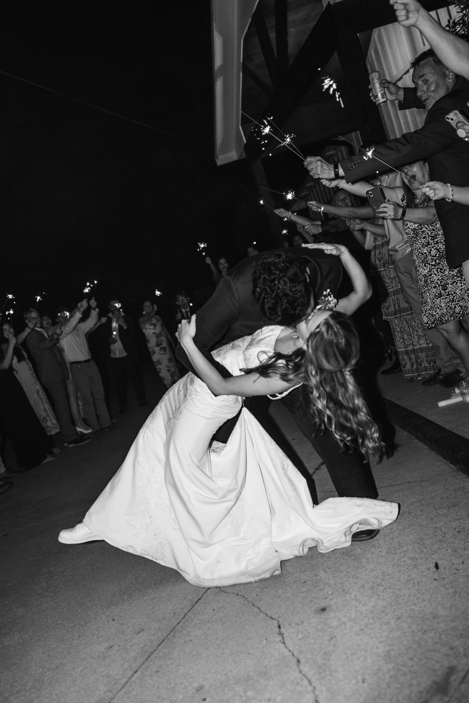 Black and white photo of a couple performing a romantic dip dance move during what appears to be a wedding reception.