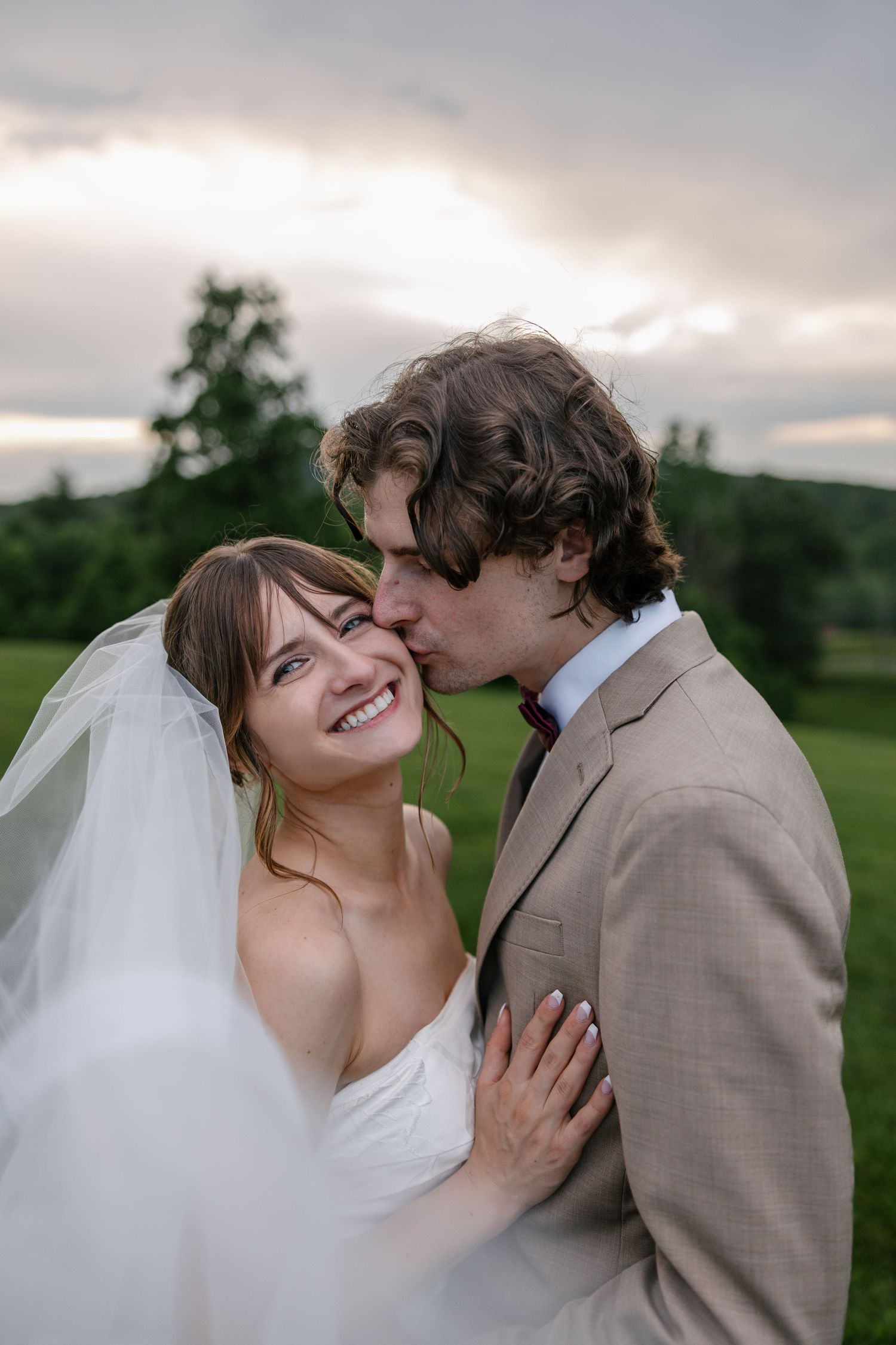 A joyful wedding moment captured outdoors with the bride in white and groom in beige sharing an intimate embrace at sunset.
