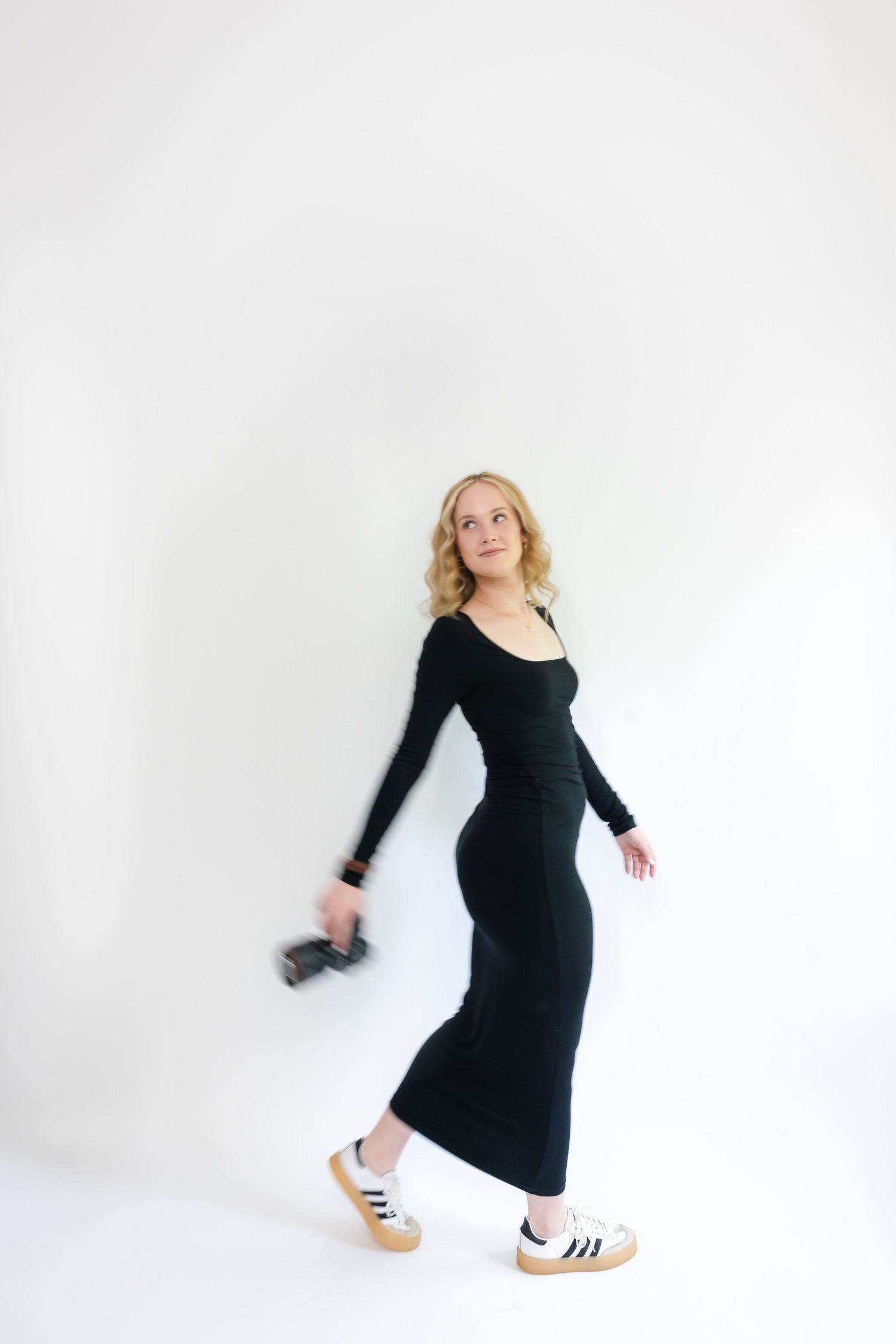 Dynamic shot of photographer in motion wearing black maxi dress and casual sneakers.