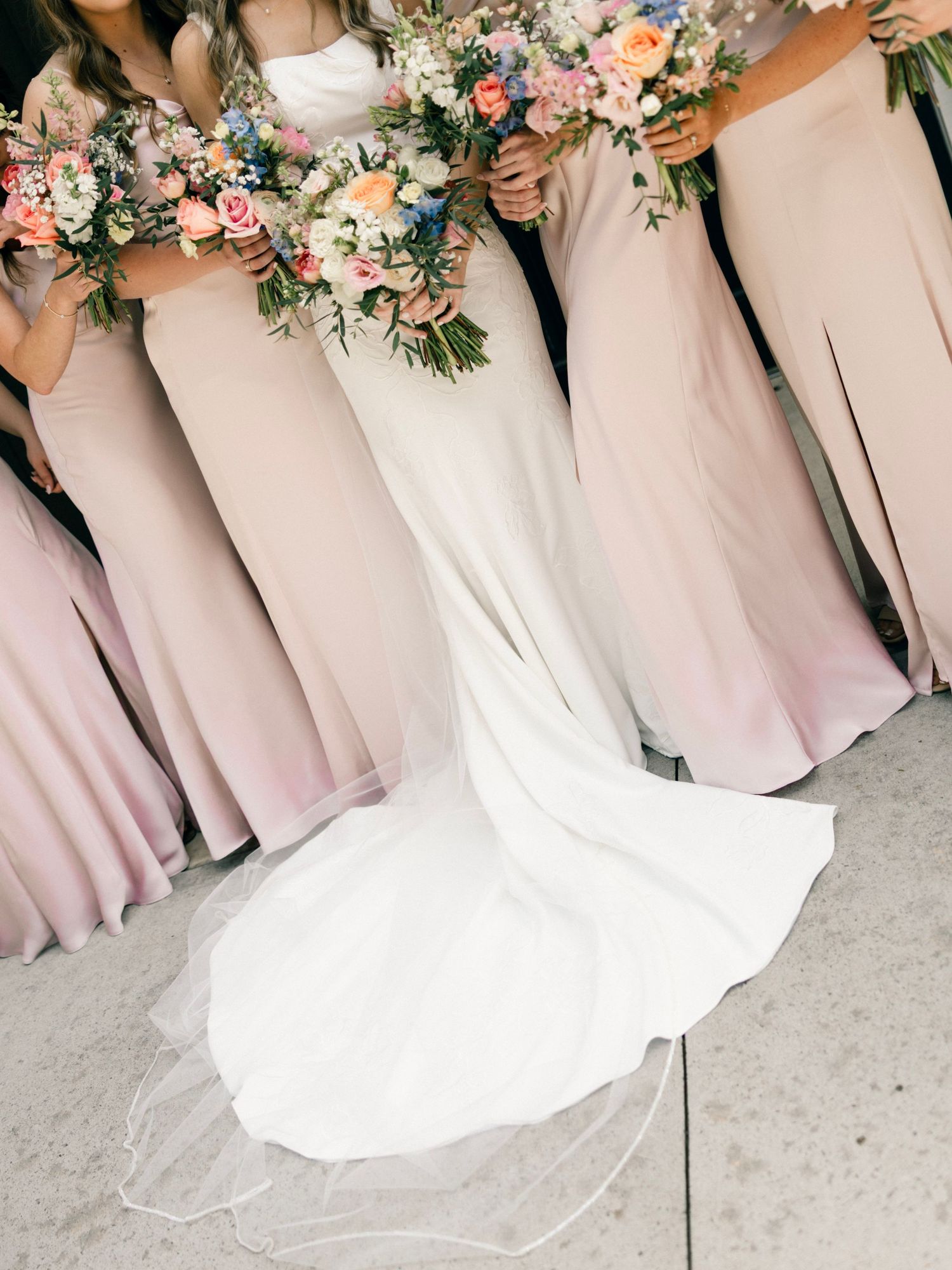 Wedding party showing dusty pink bridesmaids dresses and white bridal gown with elegant floral bouquets.