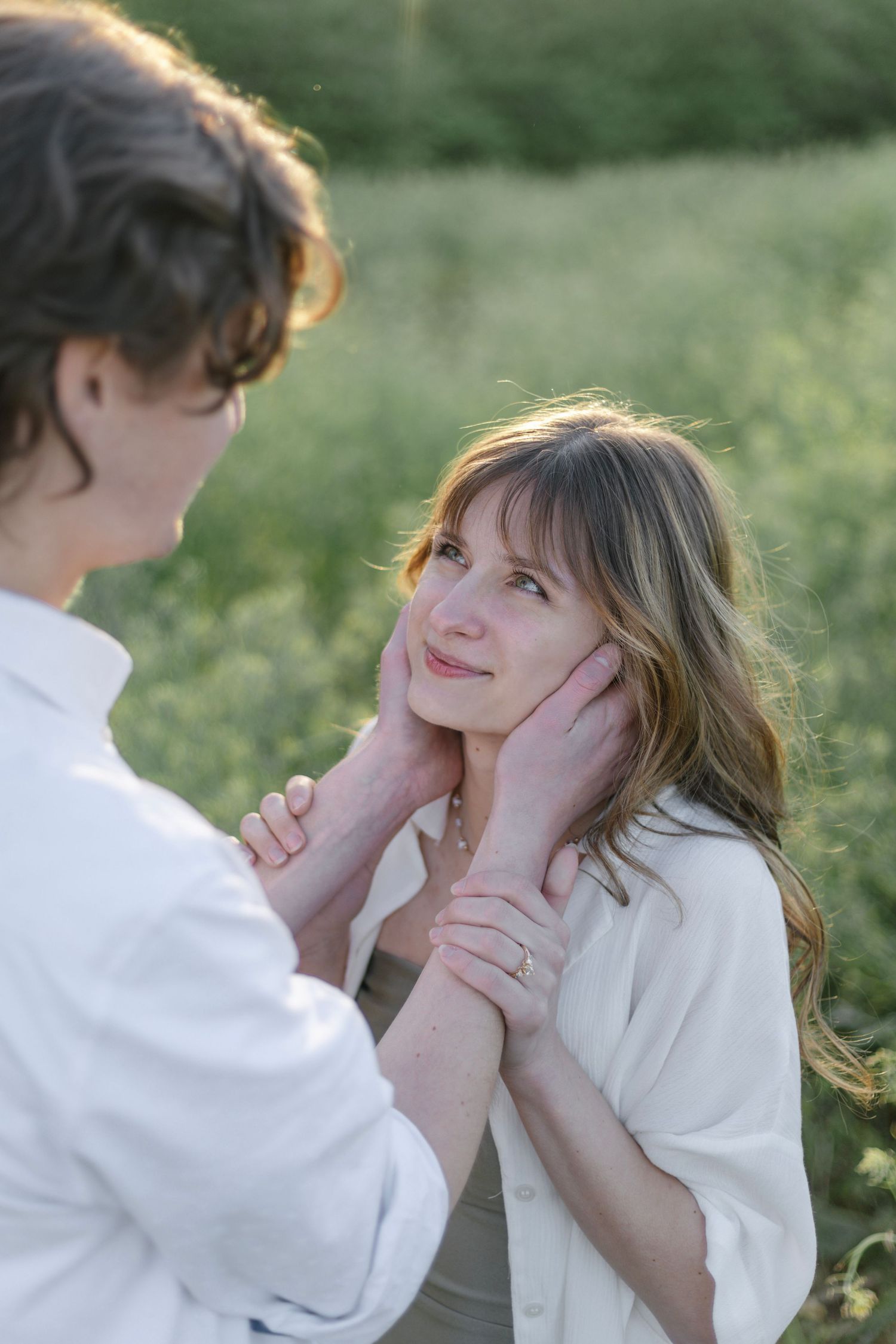 A tender romantic moment between a couple in white clothing standing outdoors in soft natural lighting.