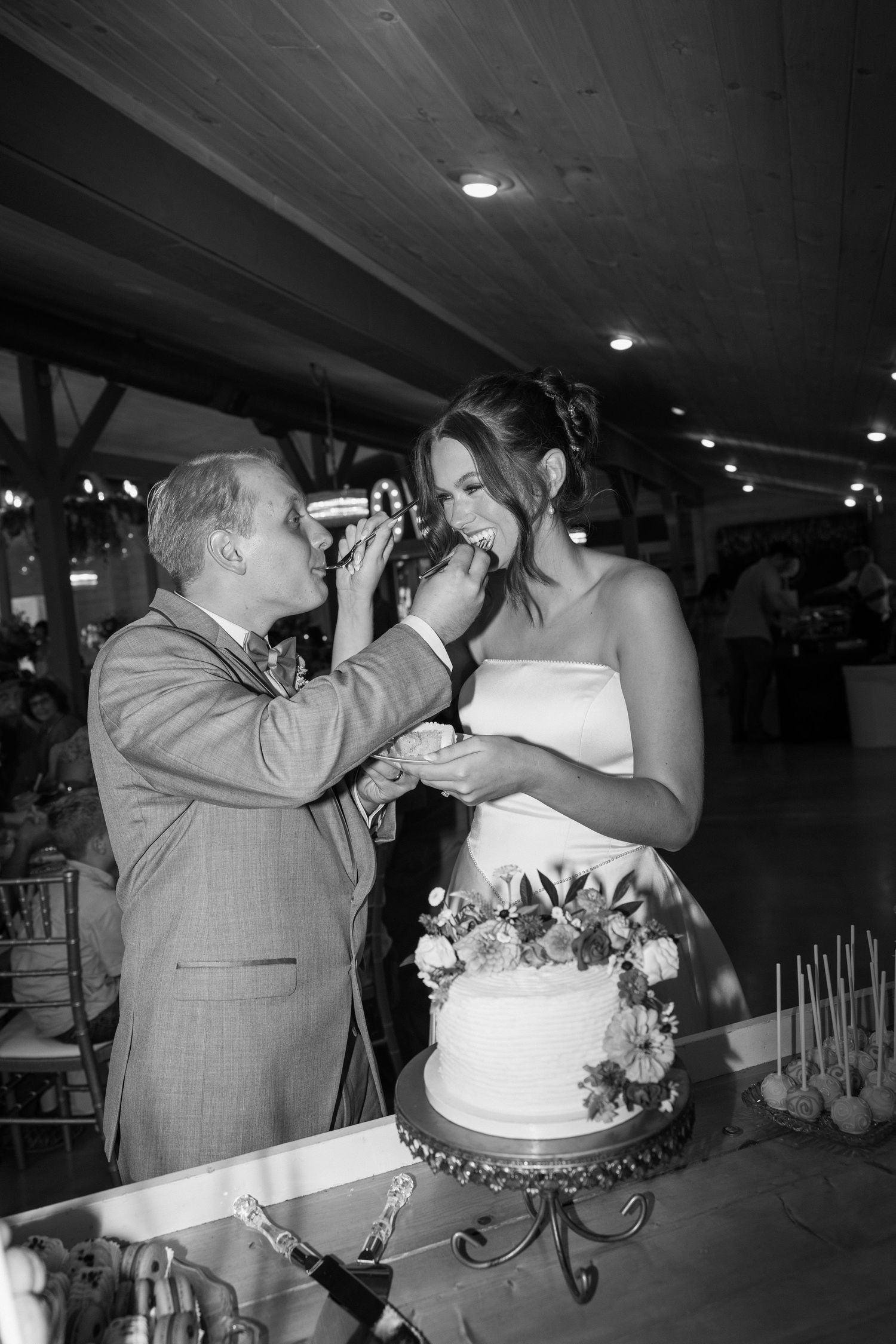 Black and white sequence of a bride and groom playfully feeding each other wedding cake at their reception.