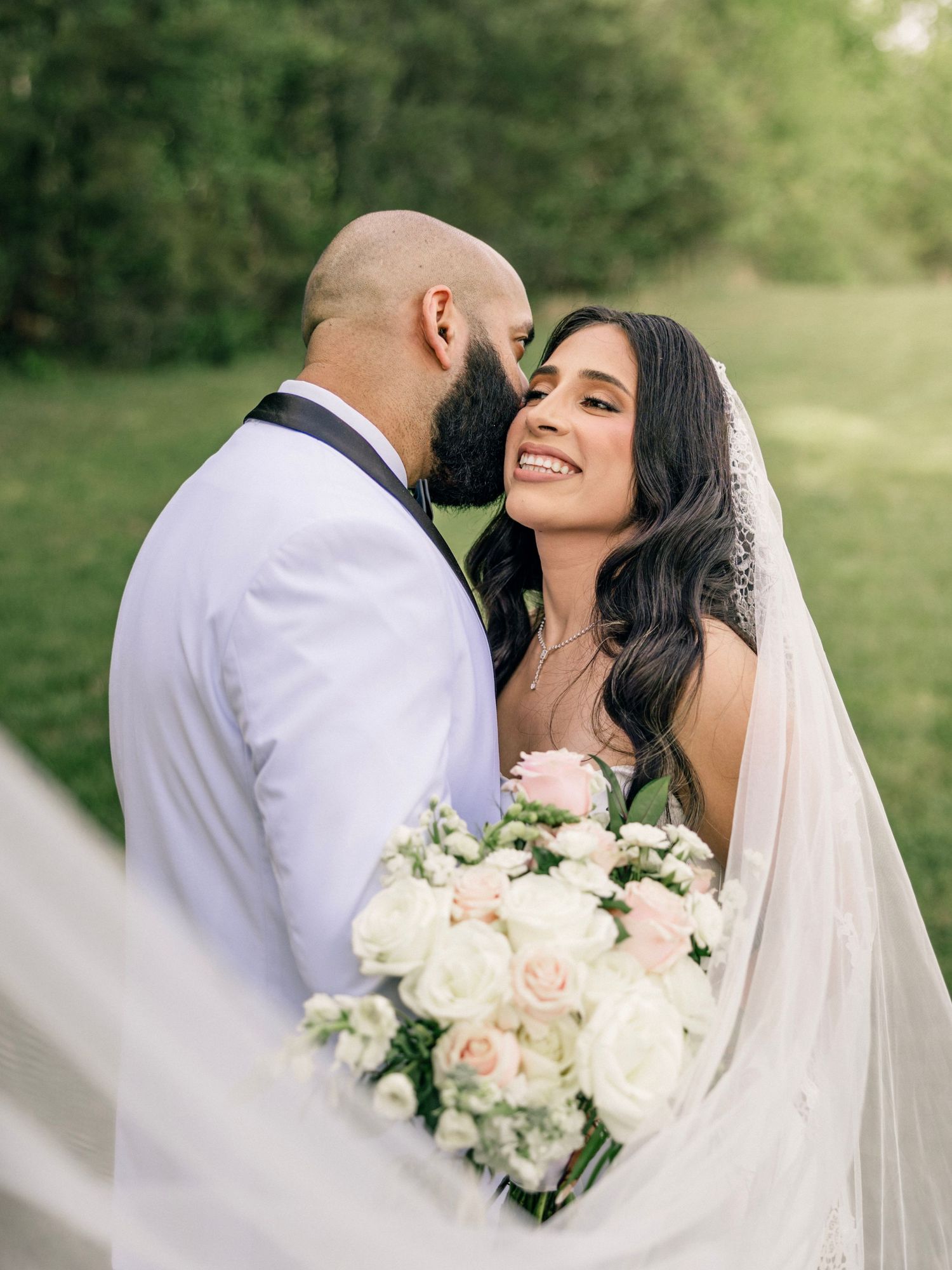 A couple shares an intimate wedding moment outdoors with a beautiful bouquet of pink and white roses.