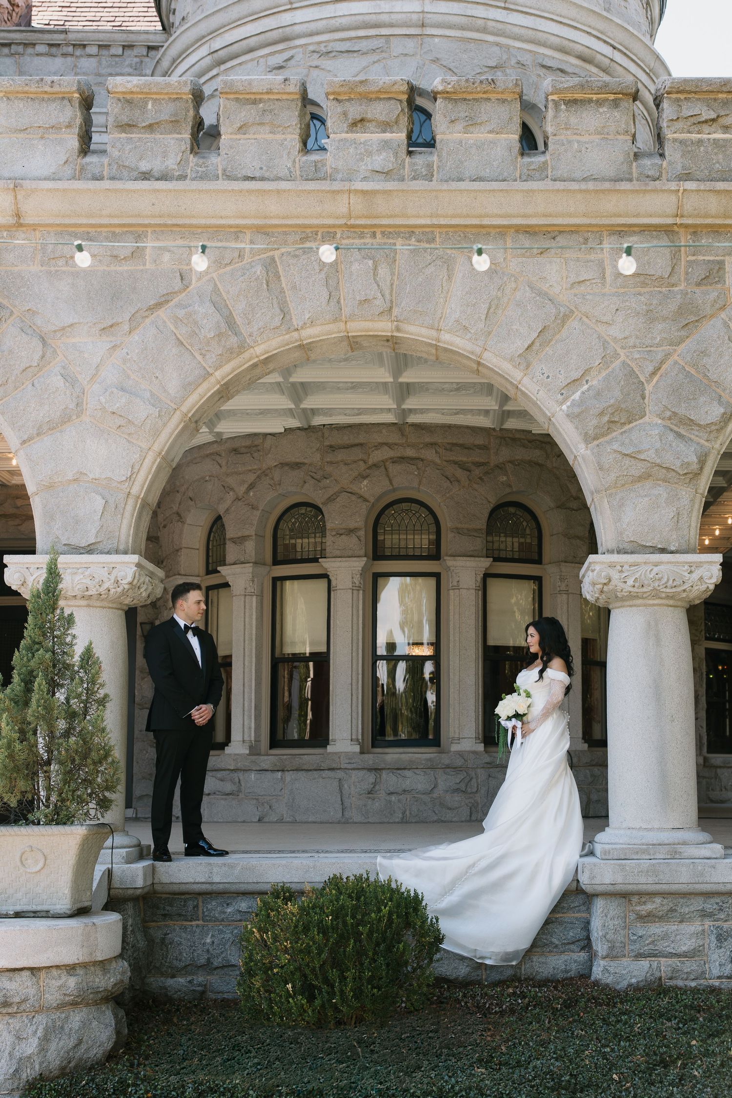 A romantic wedding photo series showing a couple posing beneath elegant stone archways at a historic building.
