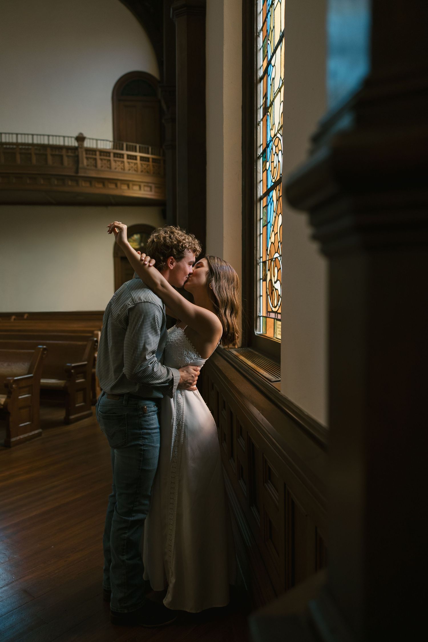 A couple sharing an intimate moment in the warm glow of light filtering through the church's stained glass windows.
