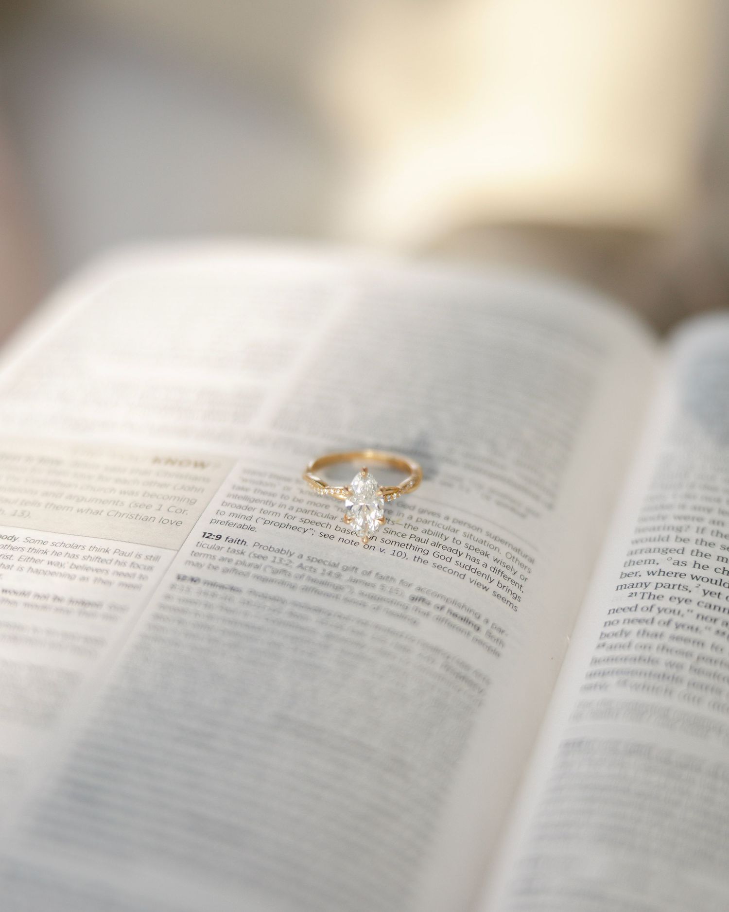 A sparkling diamond engagement ring rests delicately on an open book with blurred text pages in soft lighting.