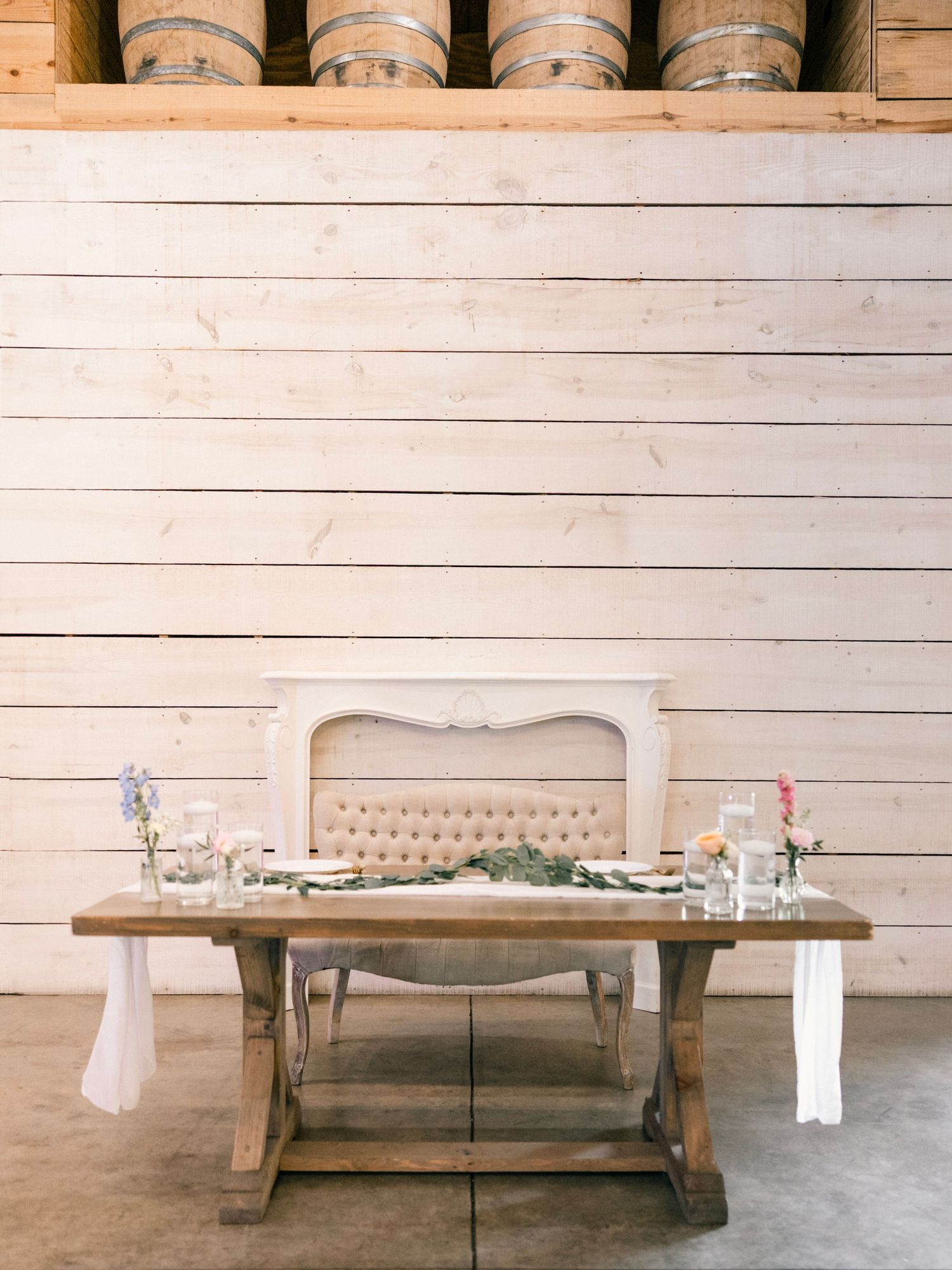 Rustic sweetheart table with wooden barrels in background displayed in elegant barn wedding setup.