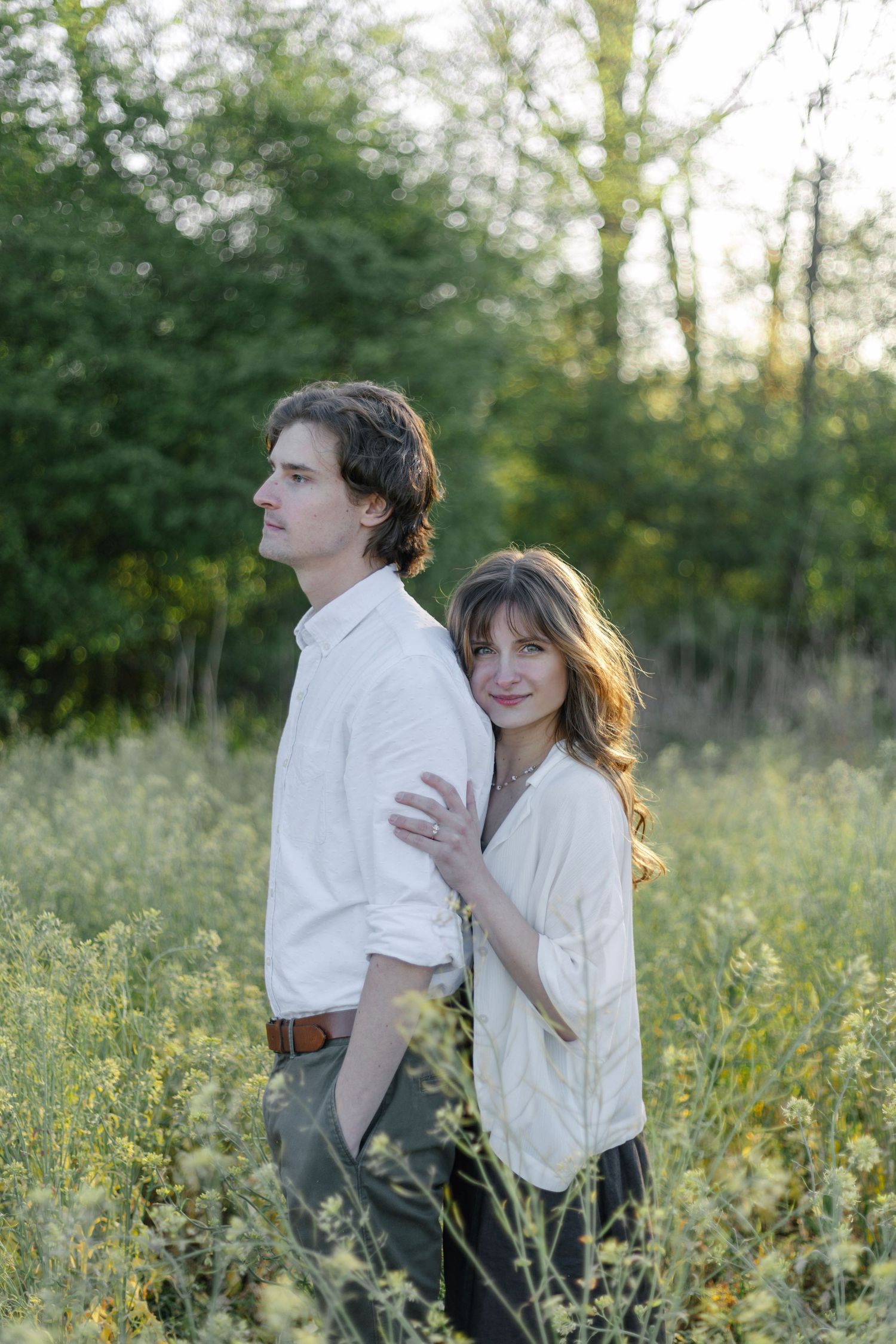 A couple in white shirts embraces while standing in a wildflower meadow at sunset.