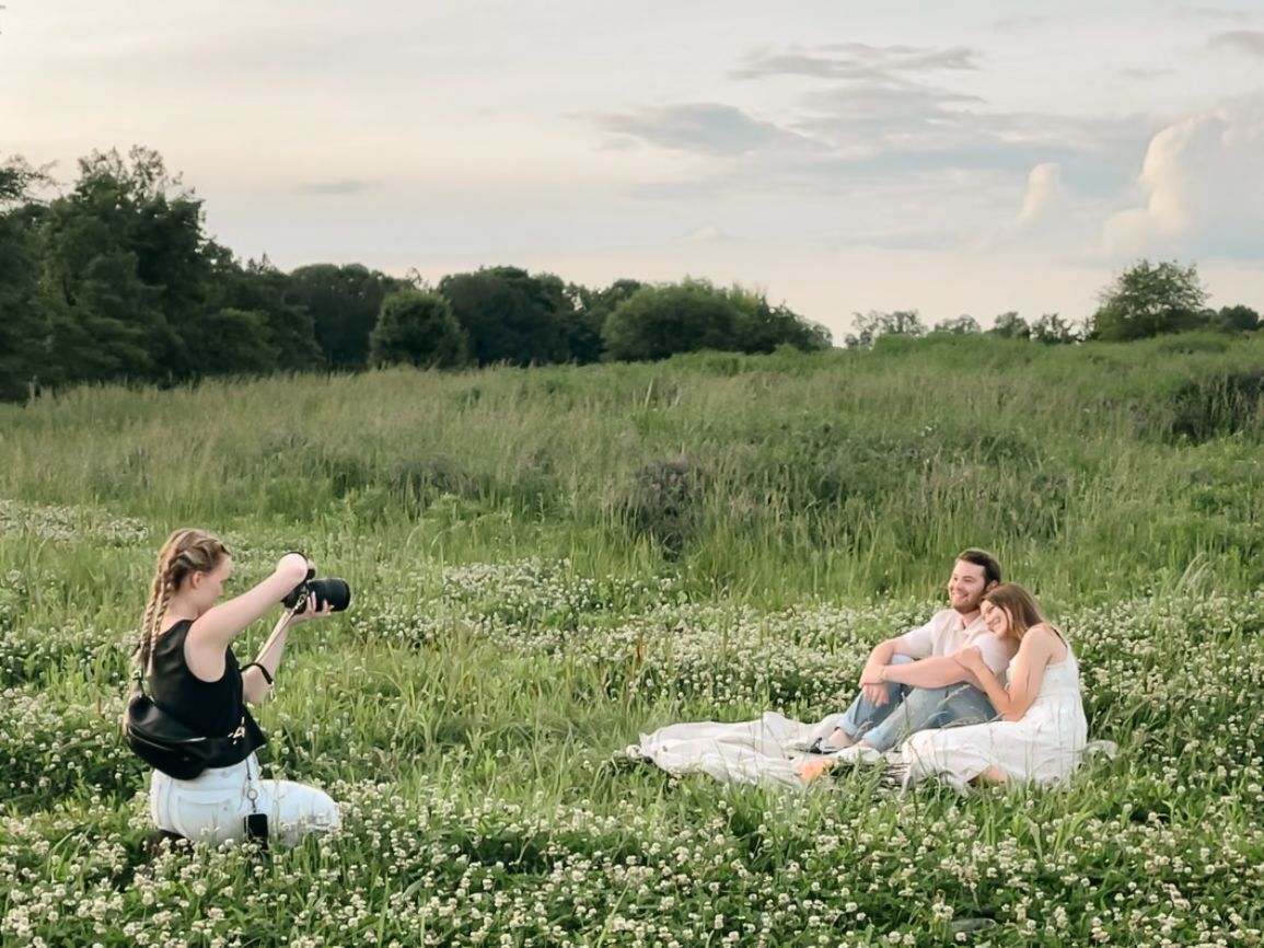 A photographer captures a candid moment as people enjoy a picnic in a wildflower meadow on a sunny day.