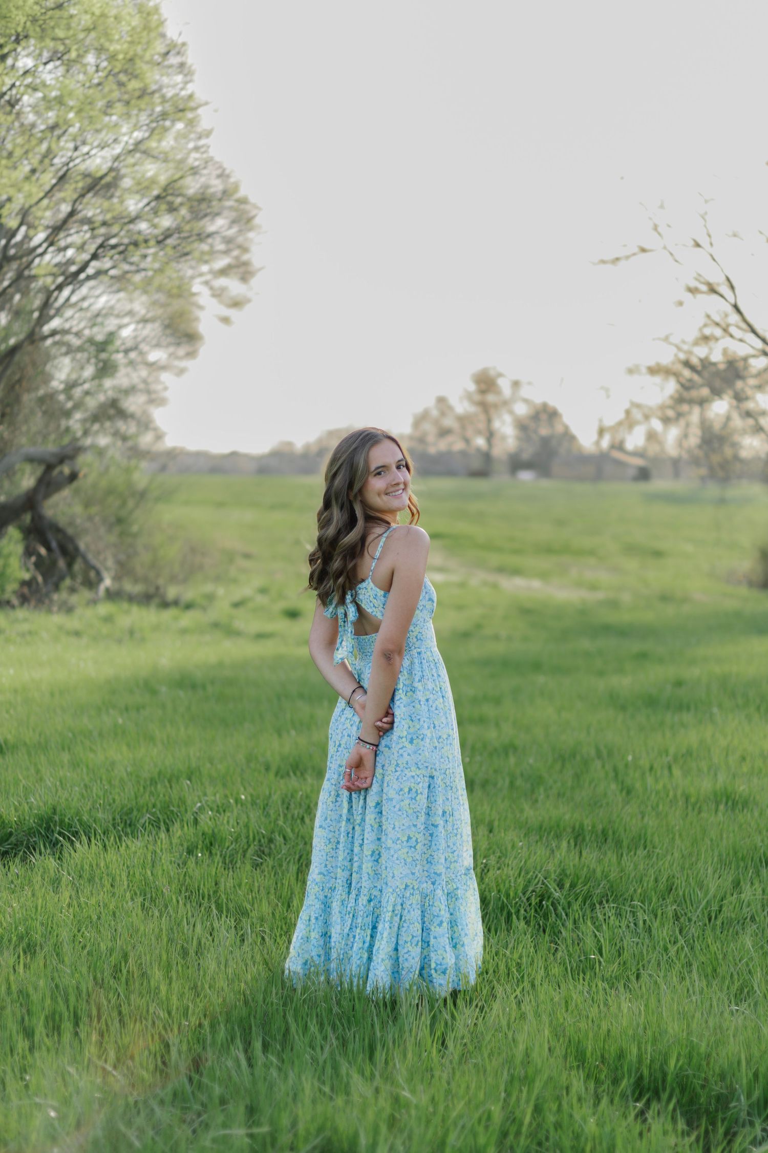 A woman in a light blue floral maxi dress poses in a green meadow during golden hour.