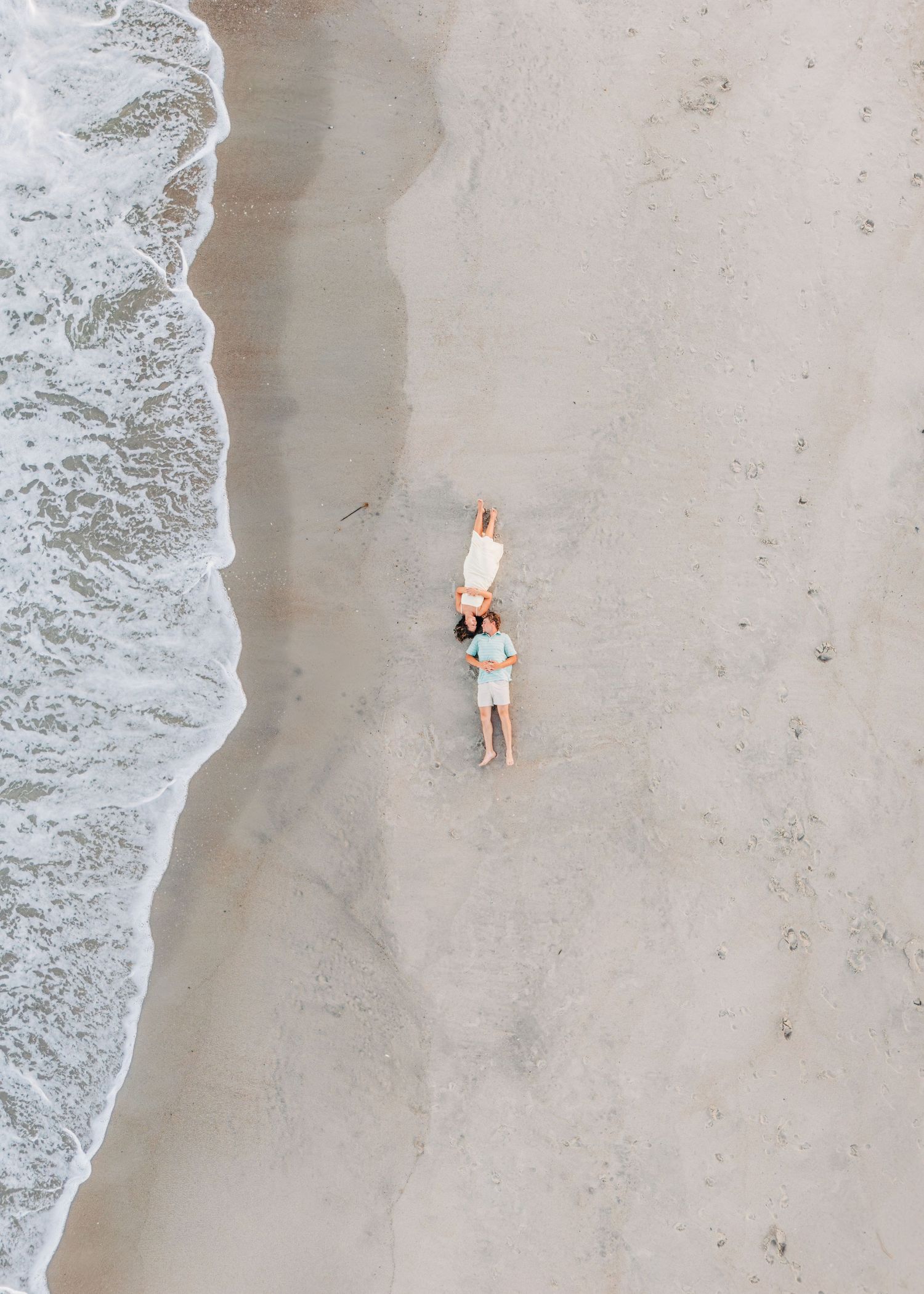 Aerial view of someone walking alone along a pristine sandy beach with white ocean waves rolling in.