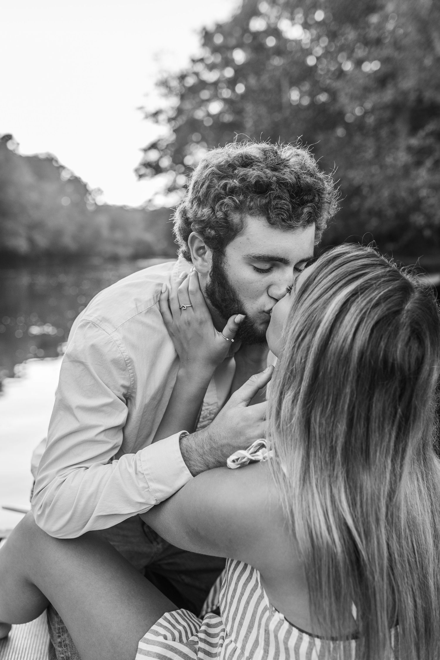 Black and white romantic portrait of couple by water at sunset.