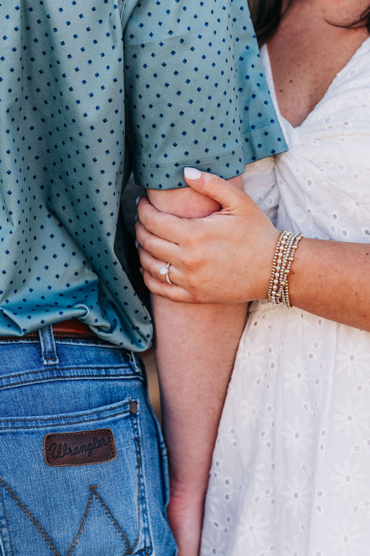 Close-up of hands showing engagement ring and bracelet with blue polka dot shirt and denim jeans.