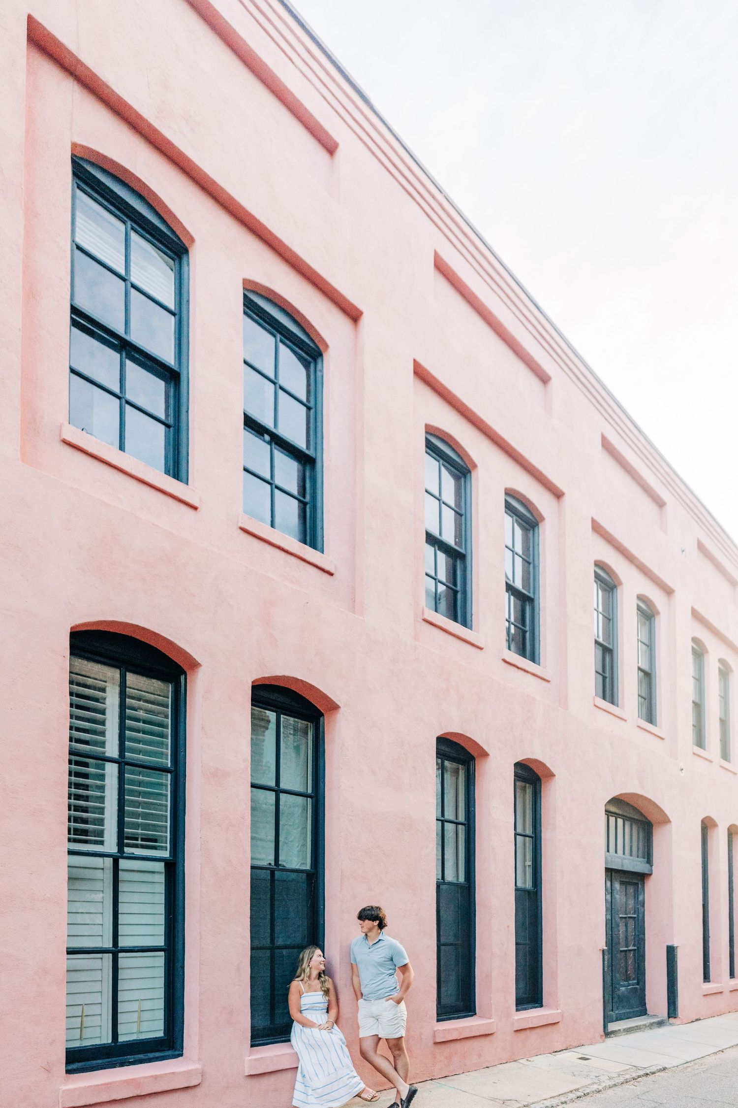 Two people sit outside a pink building with tall blue windows and arched architectural details in Charleston.
