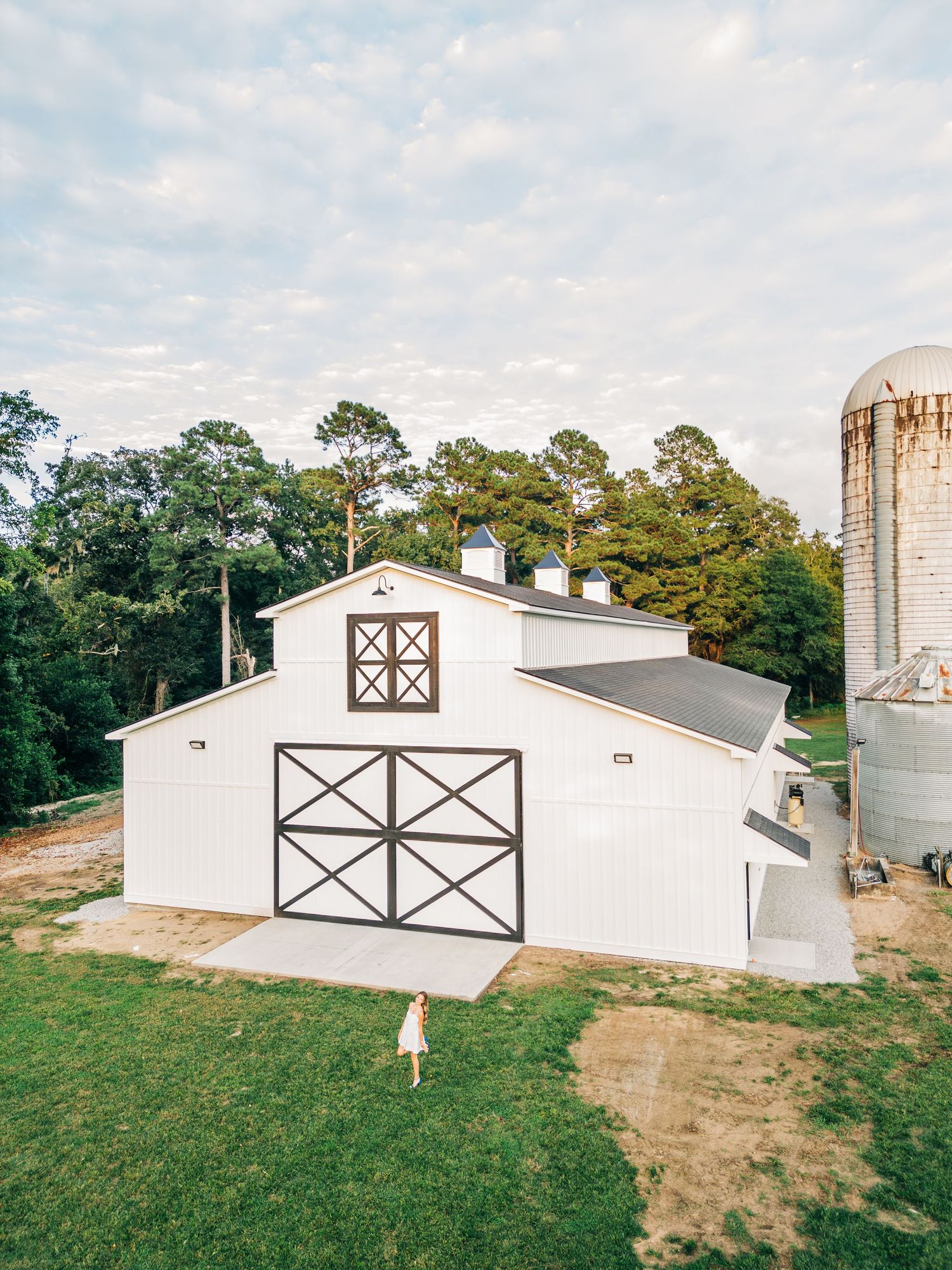White barn with cross-beam design and tall silo photographed from above.