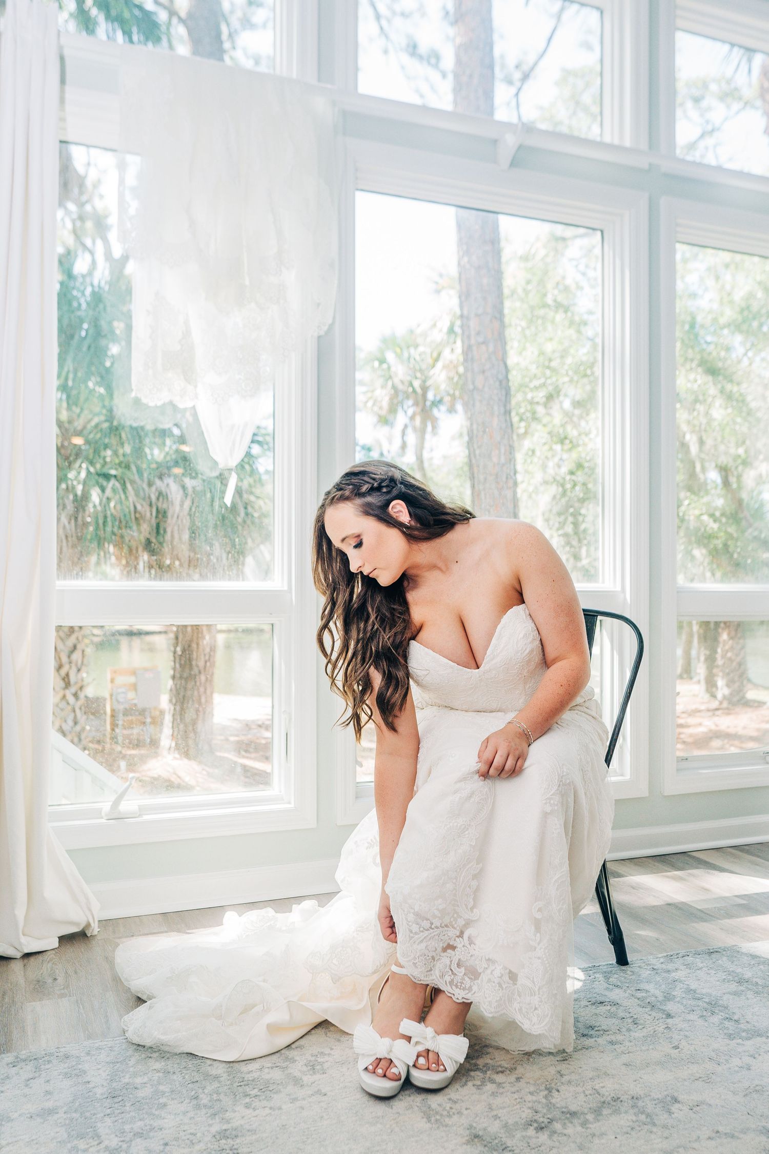 White bridal shoes being put on in a sunlit room with large windows.