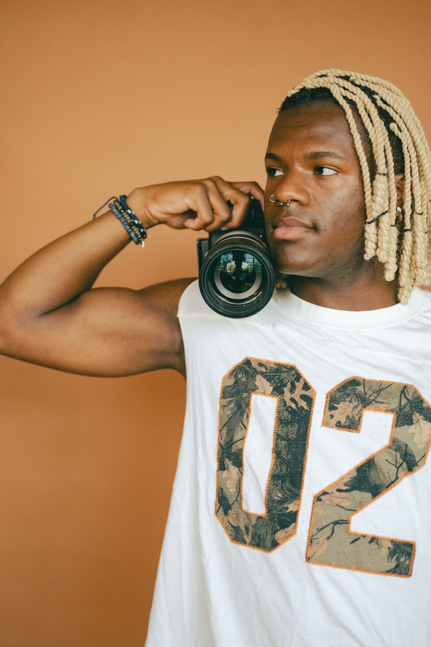 Portrait of photographer holding camera lens wearing white t-shirt against orange background.