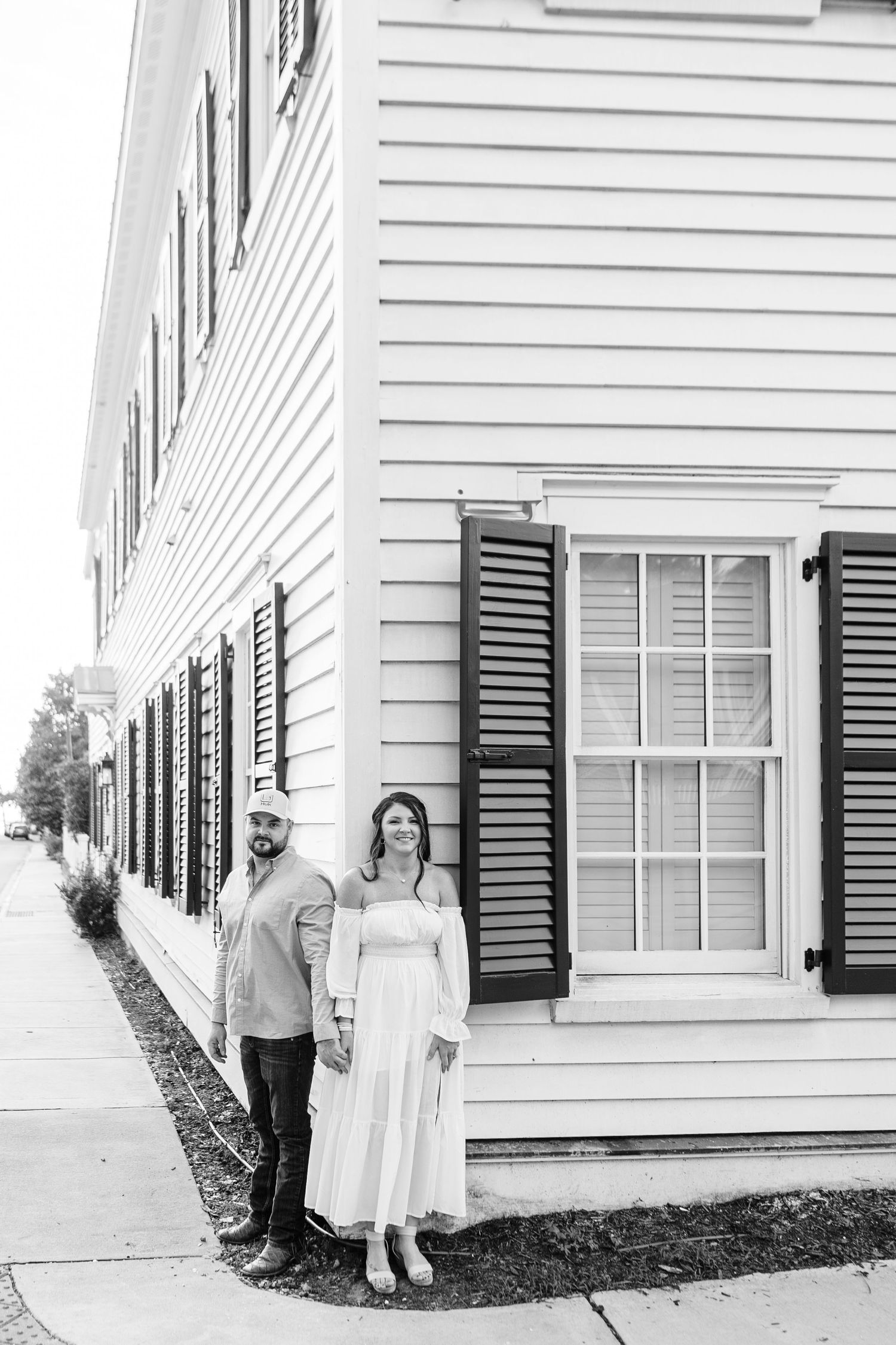 Classic black and white portraits of a couple posing against white house with black shutters.