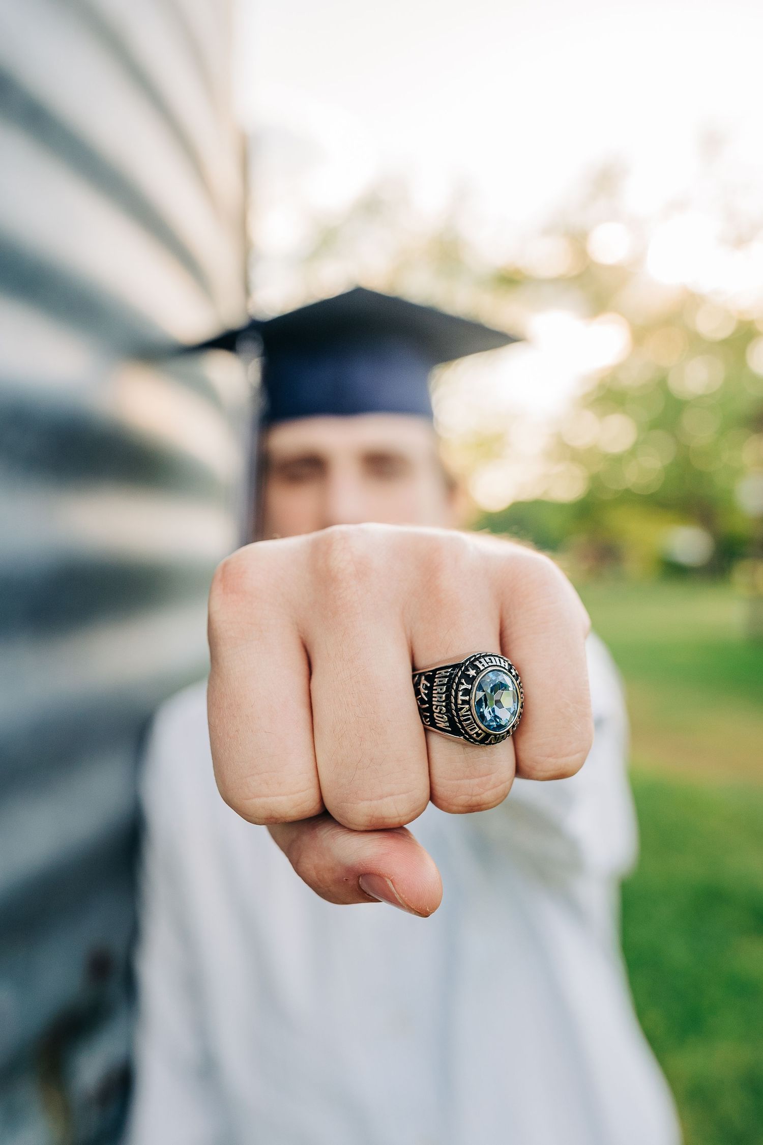 Graduate shows off class ring while wearing cap and gown outdoors.