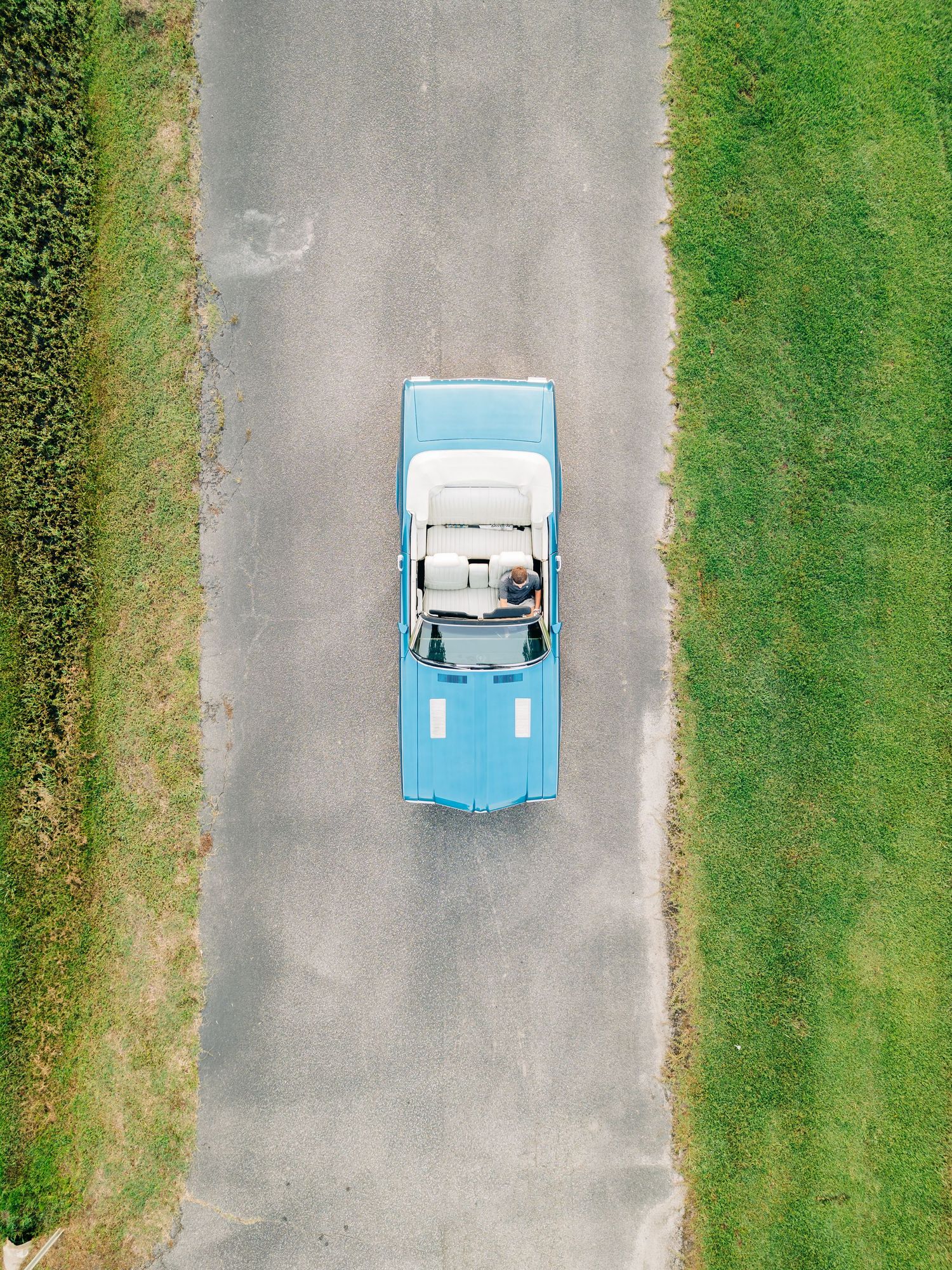 Aerial view sequence of a light blue vintage car driving through a parking lot with green grass.