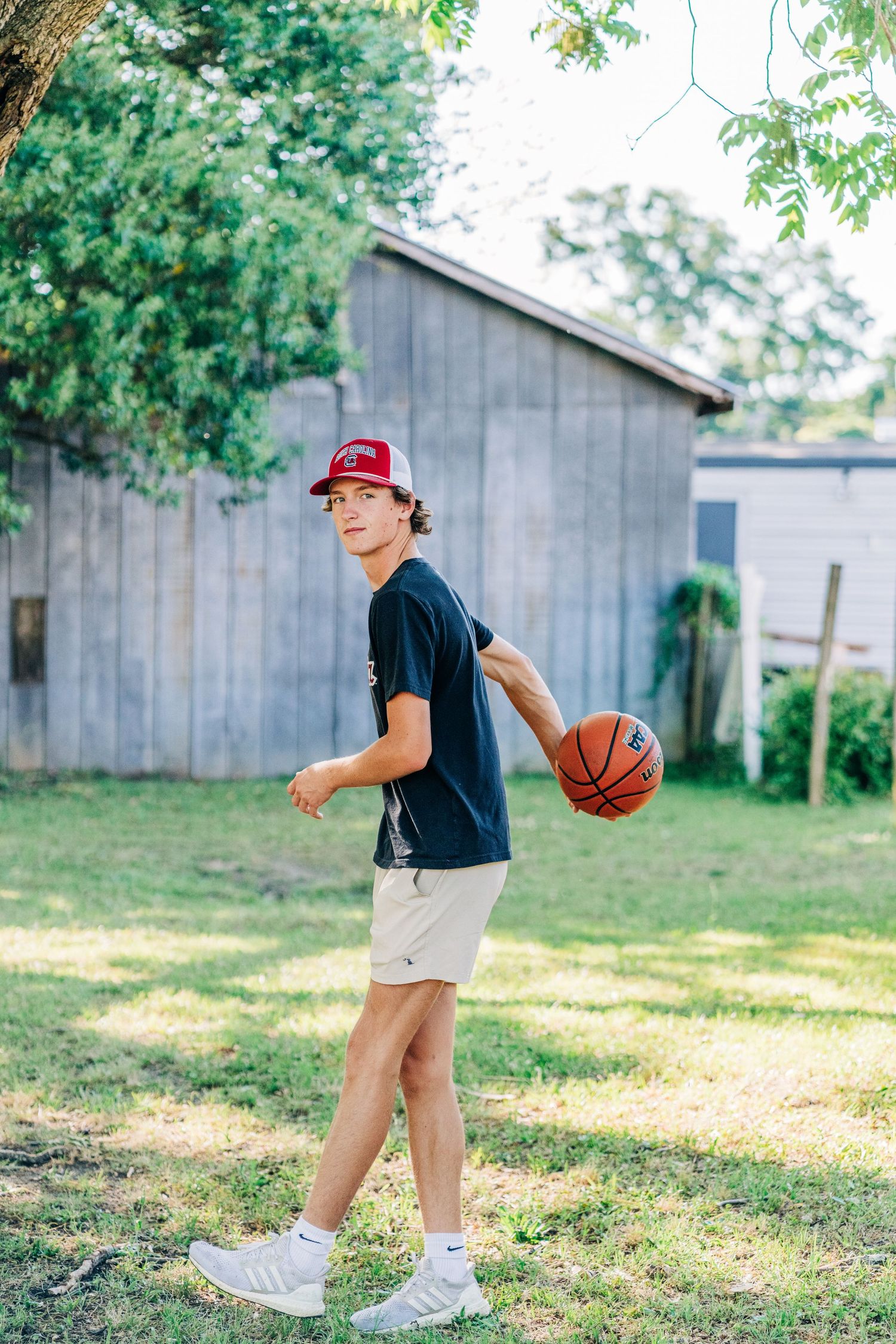 Young athlete in casual wear poses with basketball in backyard setting.