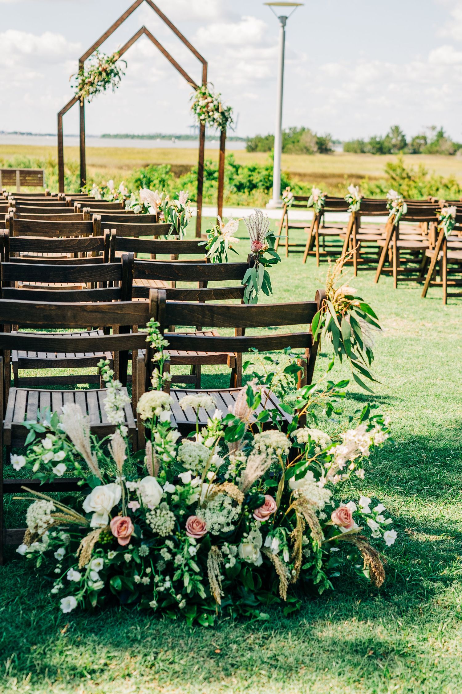 Rustic outdoor wedding ceremony setup with wooden benches and floral arrangements in a grassy field.