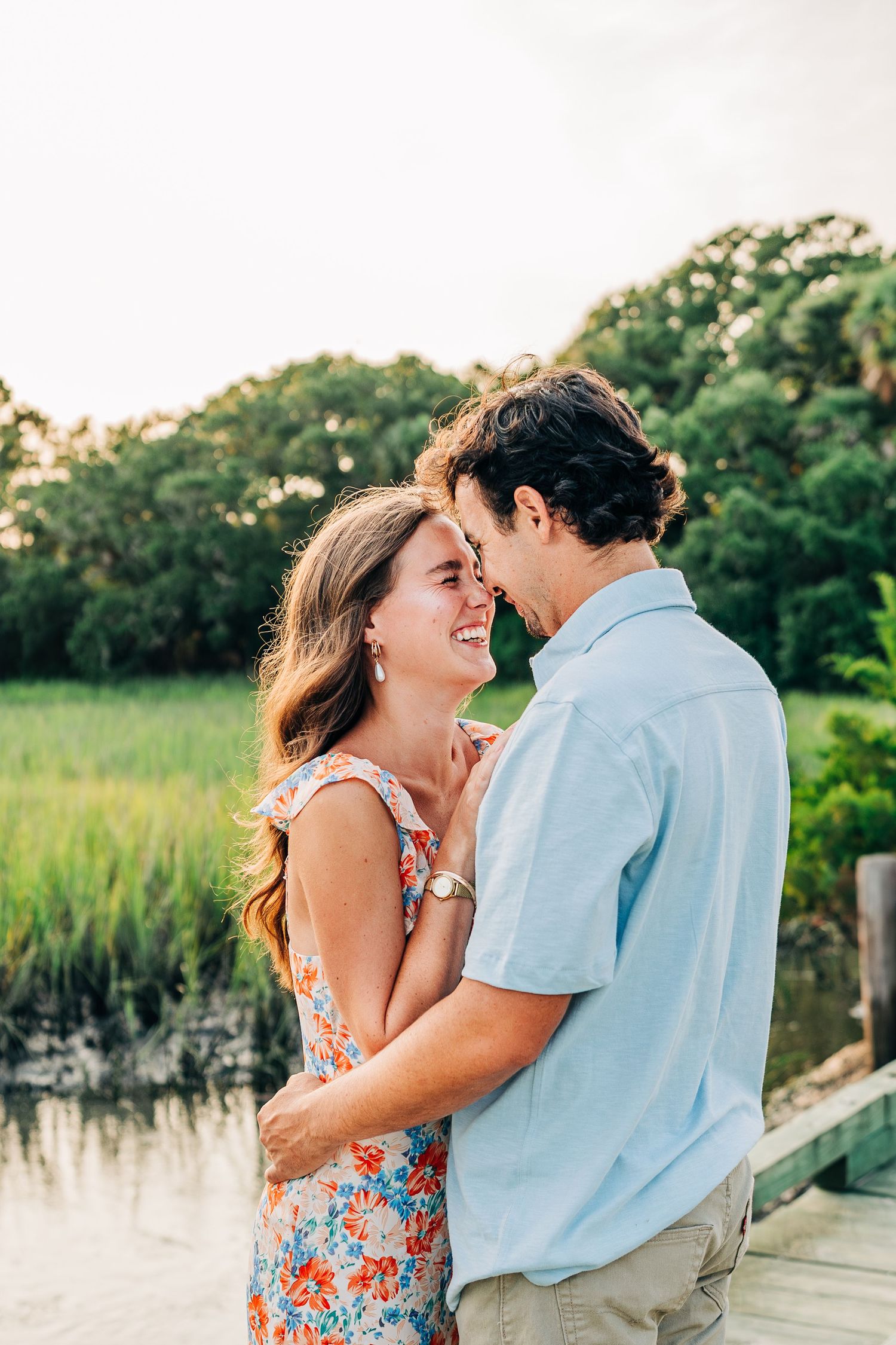 Couple sharing intimate moments on wooden dock with marsh grass and water in background.