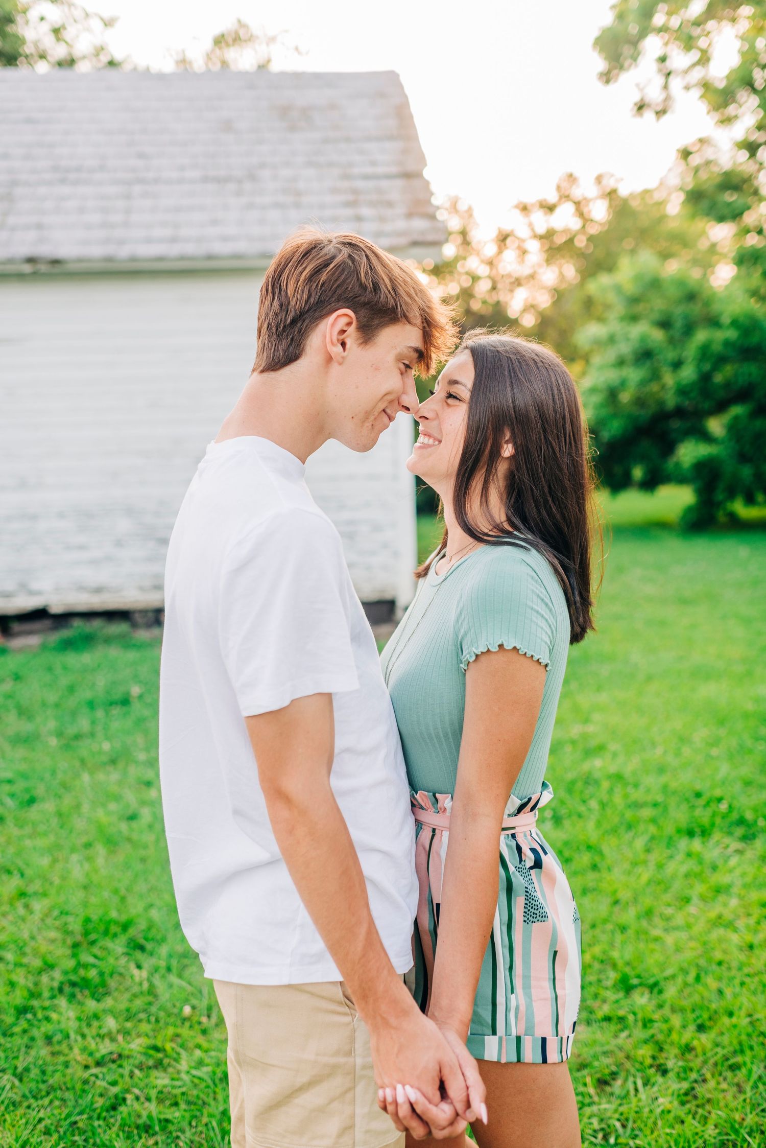Couple in casual outfits sharing intimate moment in front of white building at sunset.
