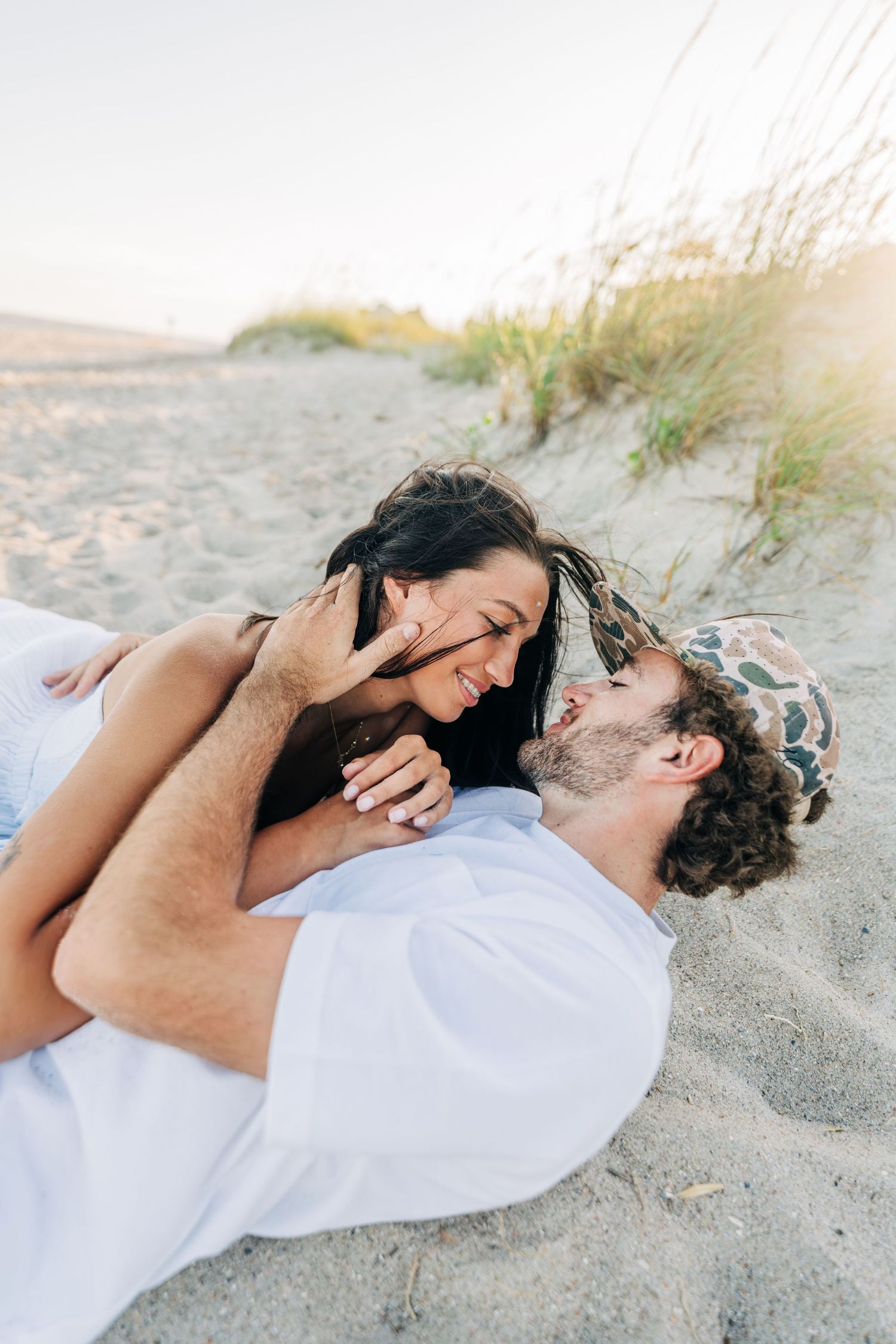 A couple shares a tender moment while lying together on a sandy beach at sunset.