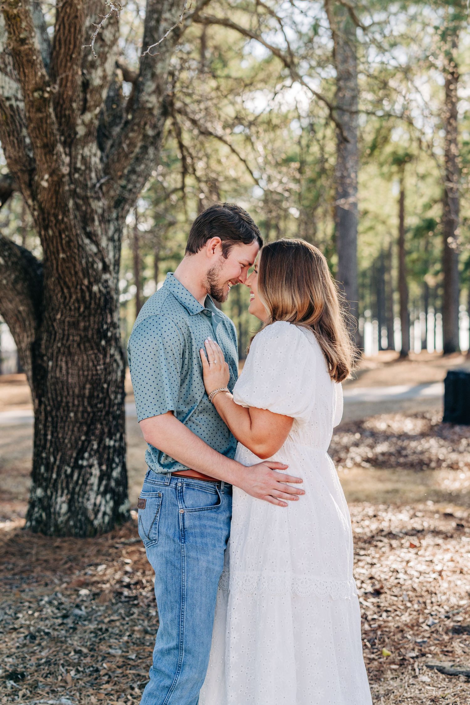 Romantic portraits of couple embracing among pine trees in wooded outdoor setting.