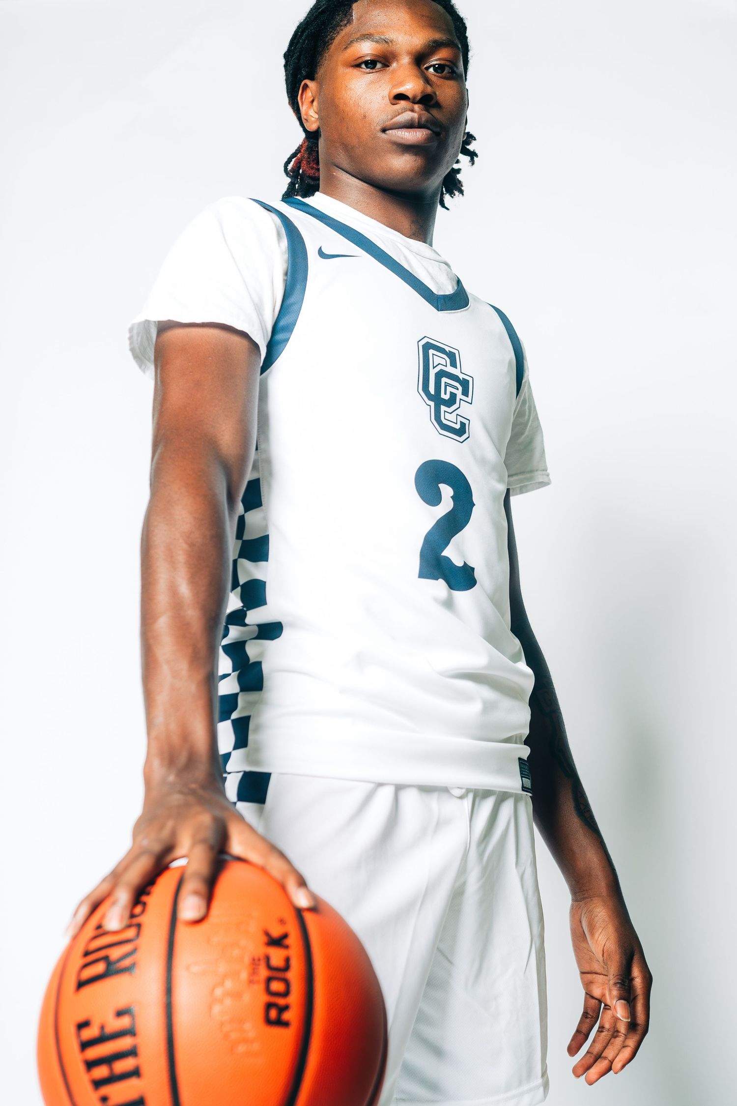 Basketball player poses in white uniform holding orange basketball.