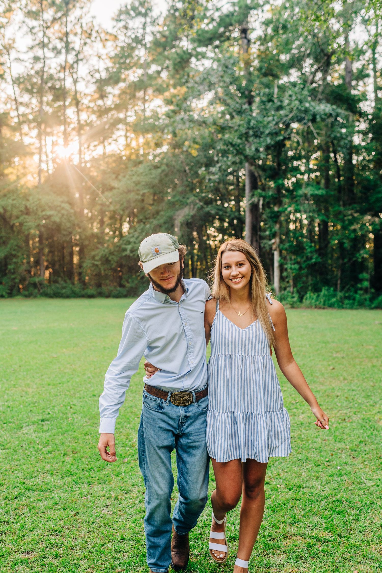 Couple walking together on grass field during sunset wearing casual summer outfits.