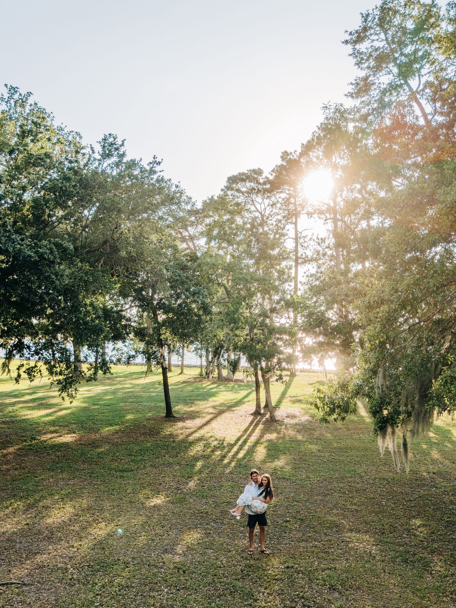 Scenic outdoor wedding venue with golden sunlight filtering through oak trees on a grassy hillside.