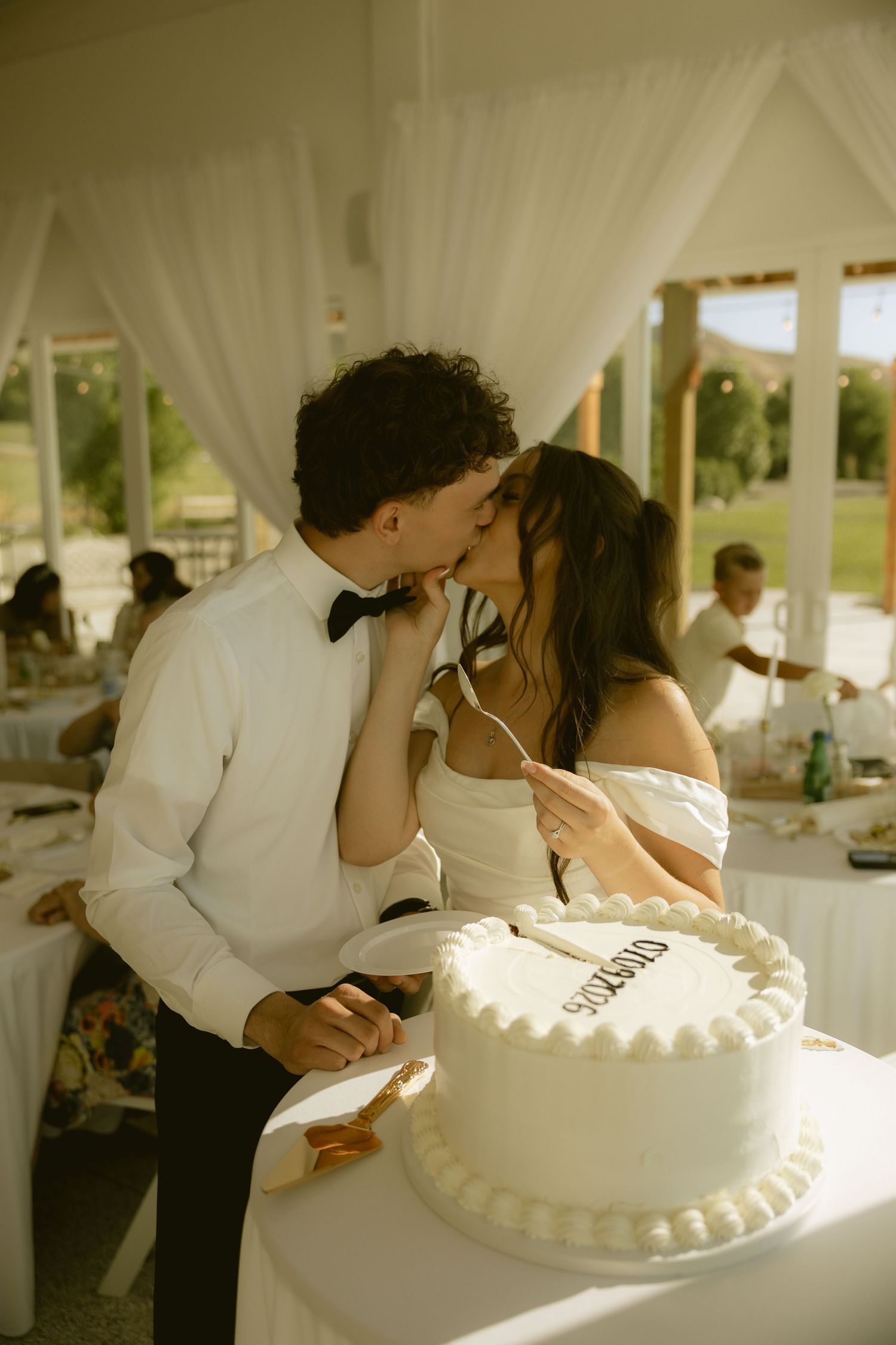 Bride and groom sharing a kiss while cutting their white wedding cake at reception.