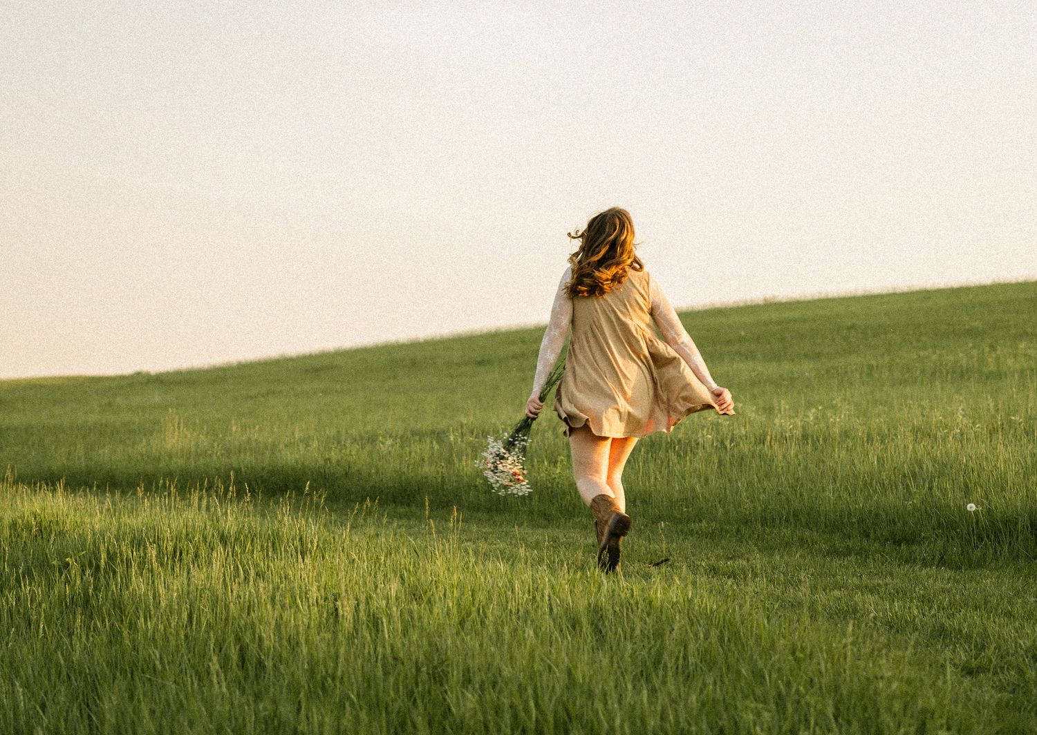 Person walking through a green meadow at sunset with distant hills in view.