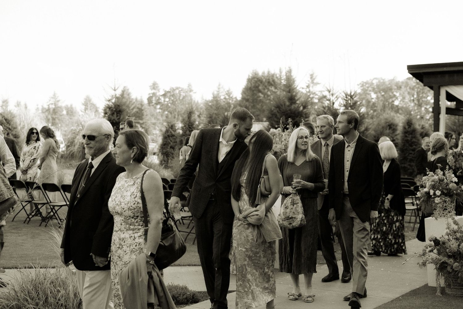 Wedding guests mingle during outdoor reception in black and white photography.
