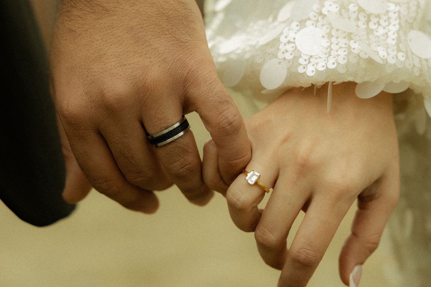 Close-up of hands displaying wedding rings against formal attire.