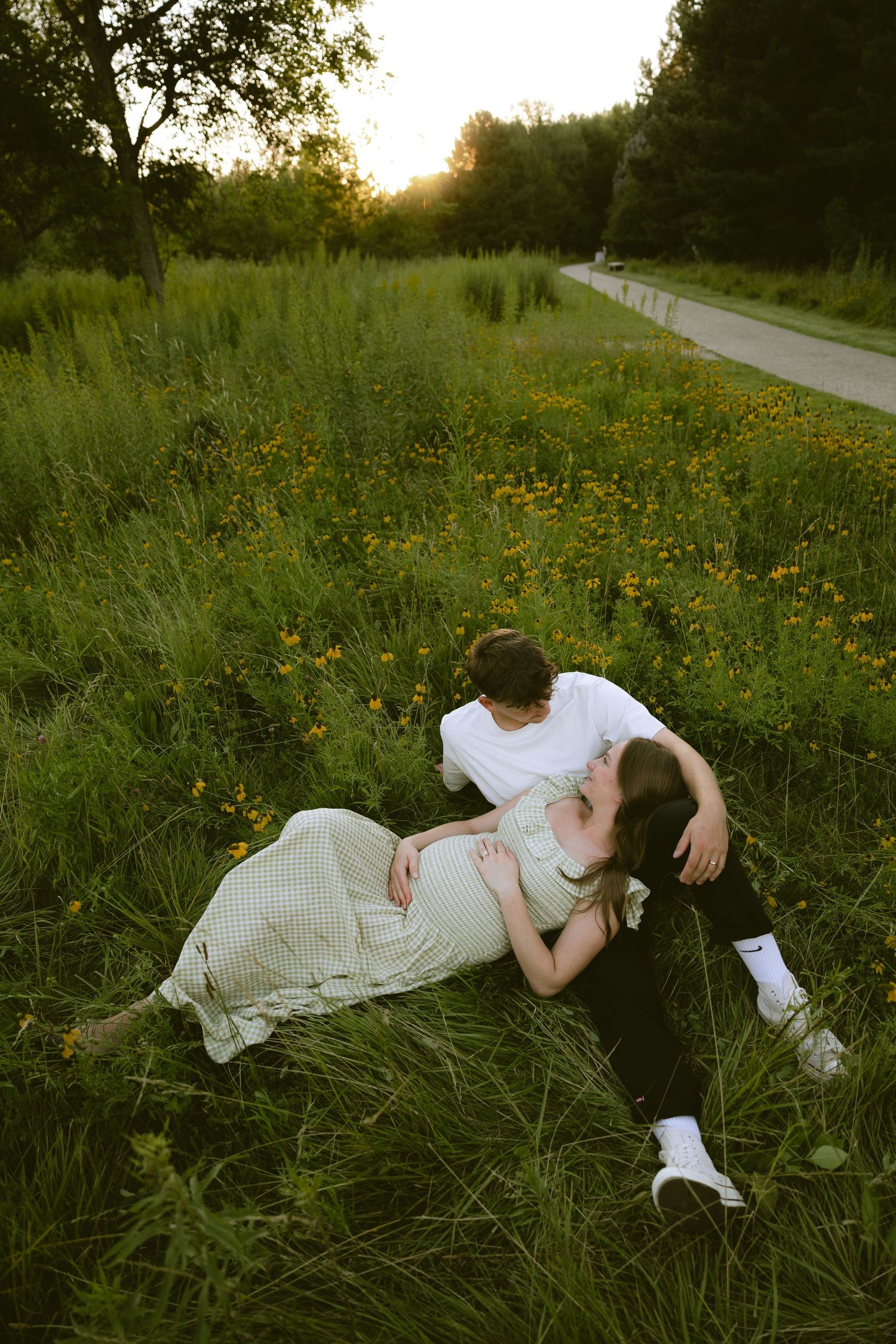 Couple relaxing in a wildflower meadow at sunset, pregnant woman in cream dress lying on partner.