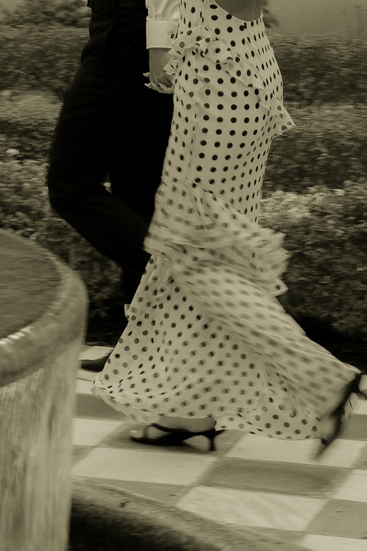 Flamenco dancer in polka dot ruffled dress performing with partner on checkered floor, sepia toned.