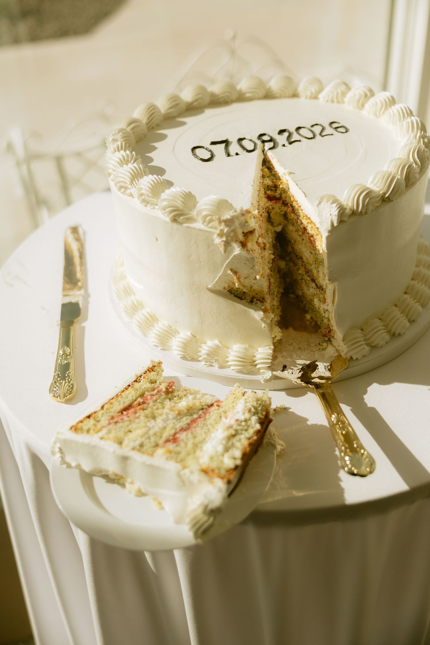 Sliced white wedding cake with 07.09.2026 date inscription on a decorated table.