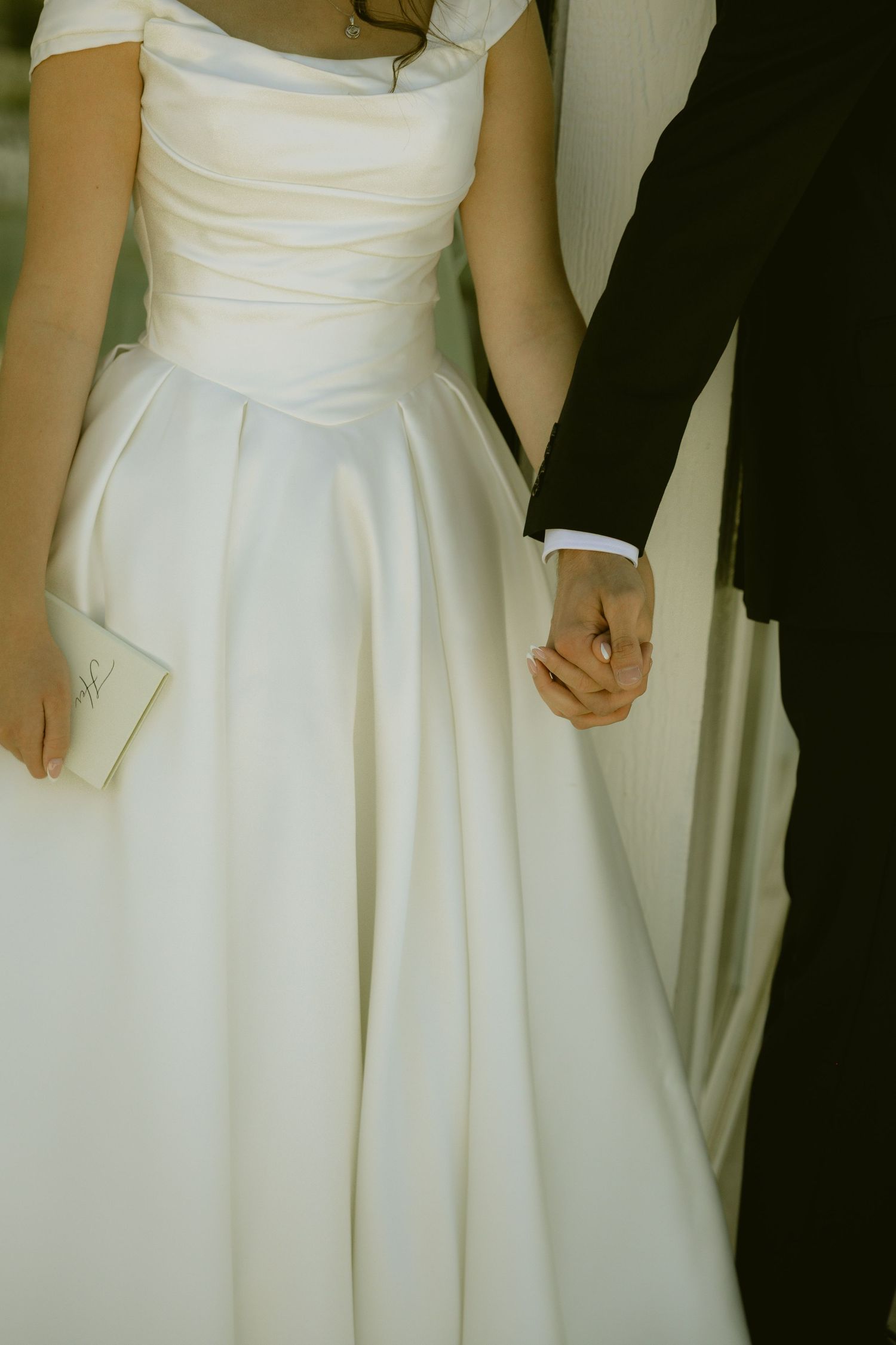 Bride in elegant white satin ball gown holding hands with groom in black suit at wedding ceremony.