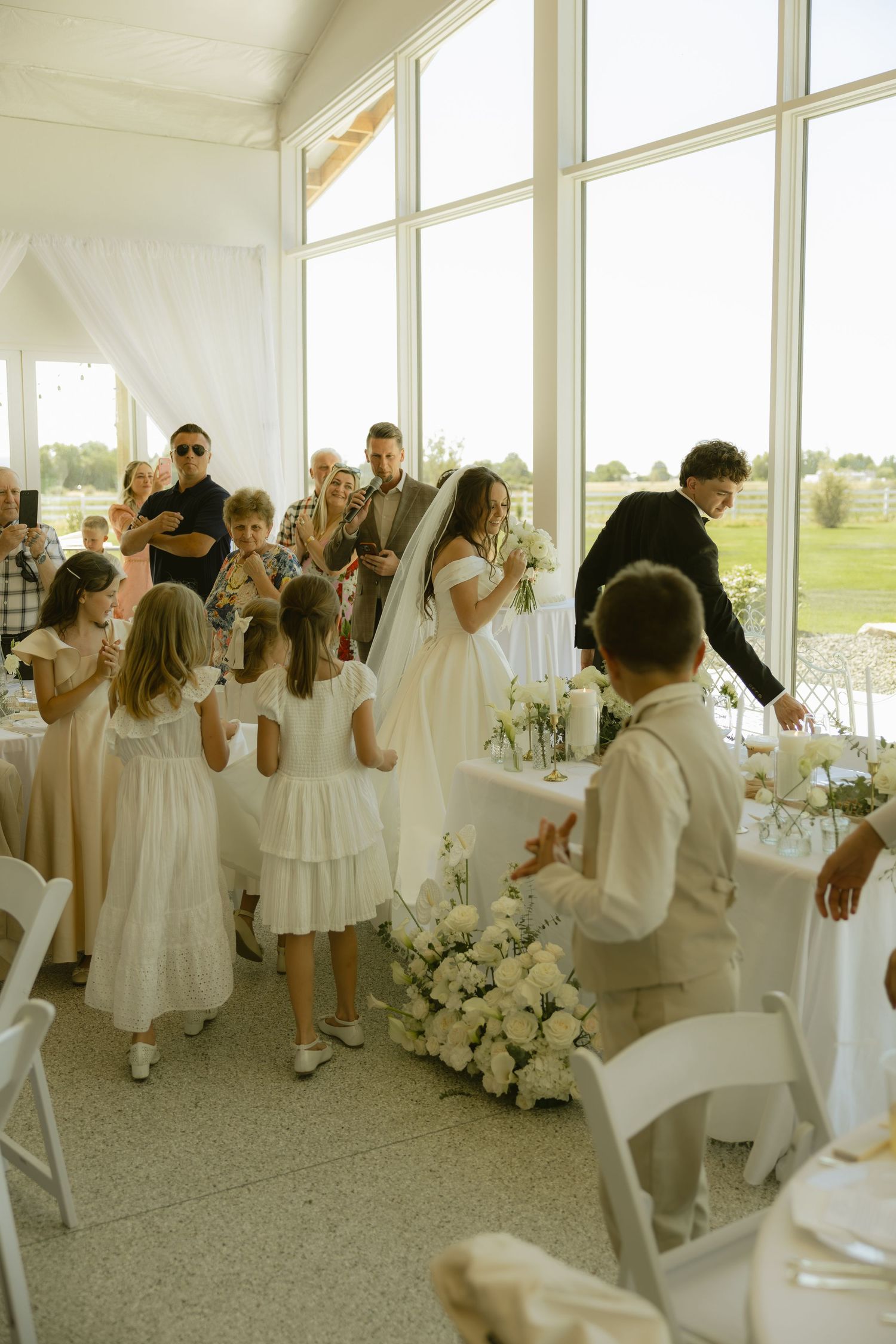 Bride in white gown and veil surrounded by flower girls in white dresses at elegant wedding reception venue.