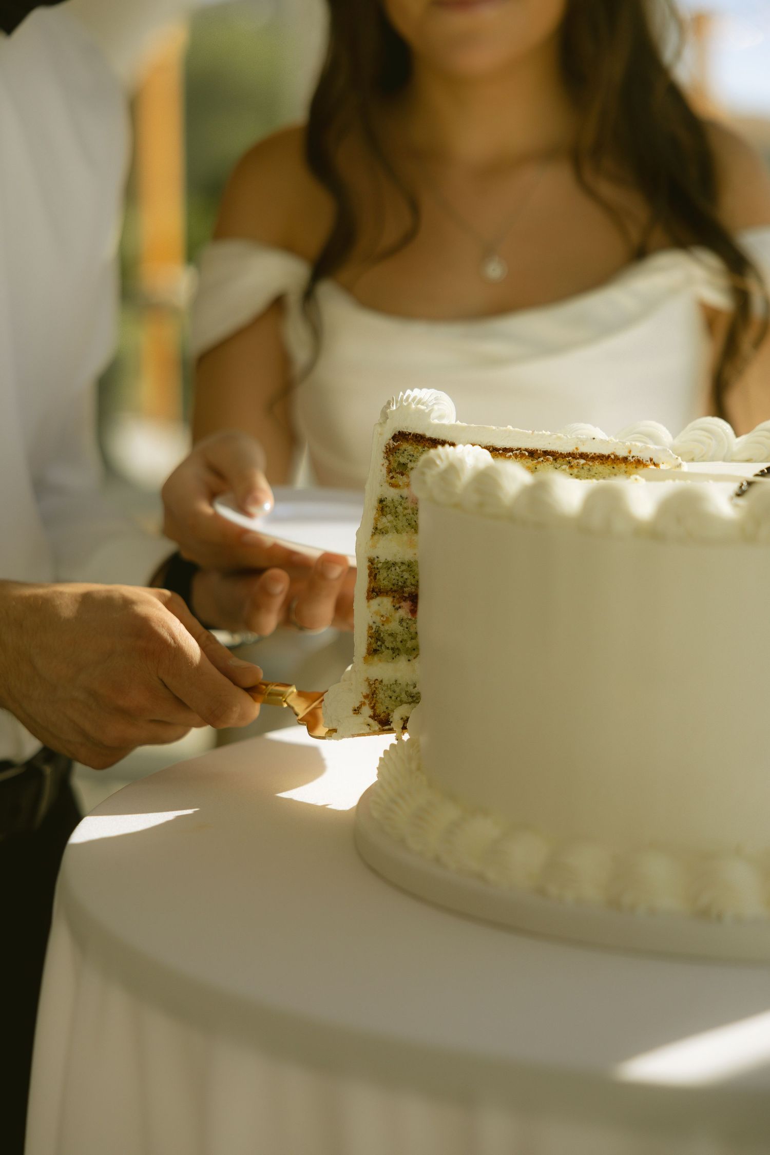 Bride and groom cutting a white wedding cake with green layers at an outdoor reception ceremony.