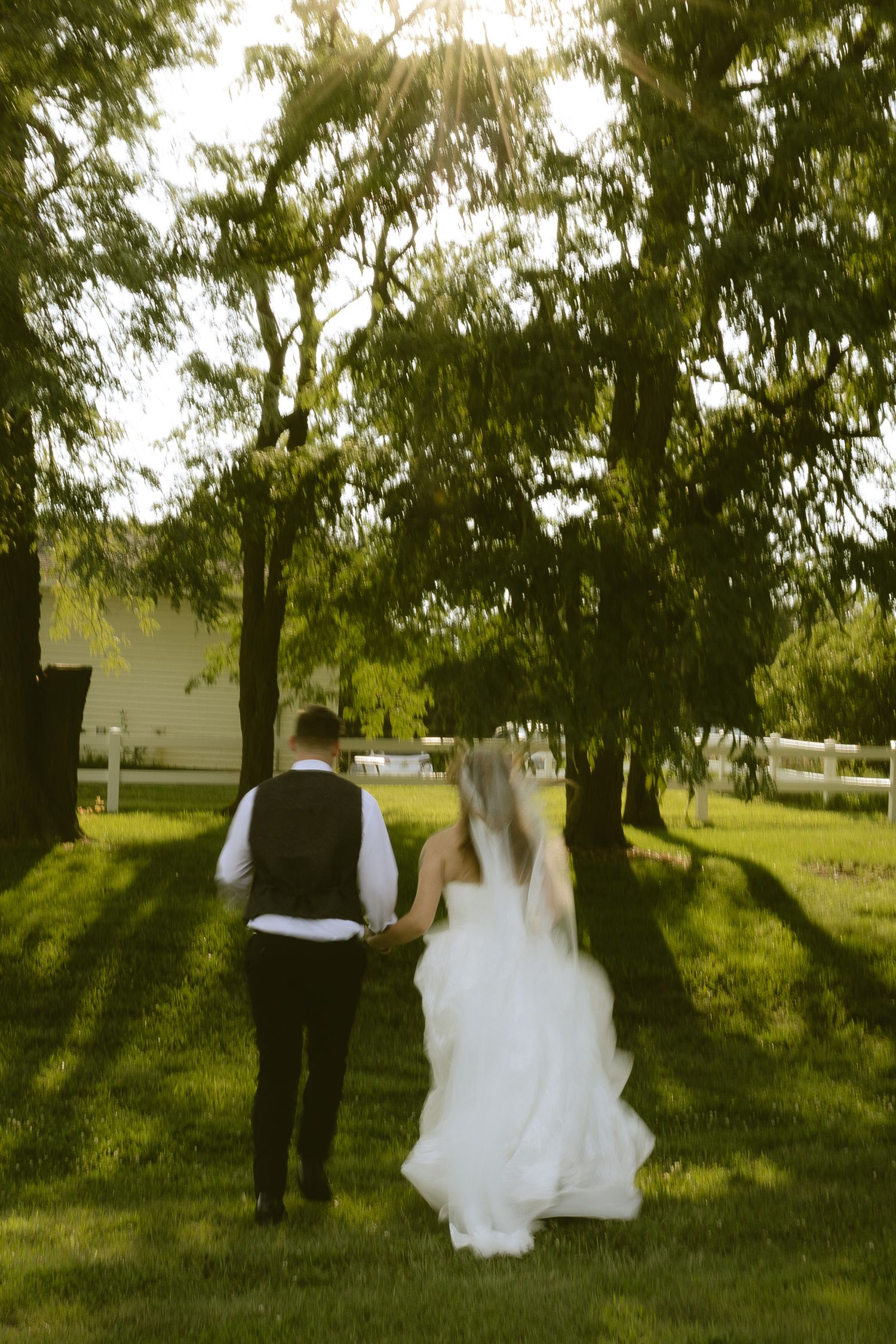 Bride and groom walking hand in hand through lush green garden during golden hour wedding celebration.