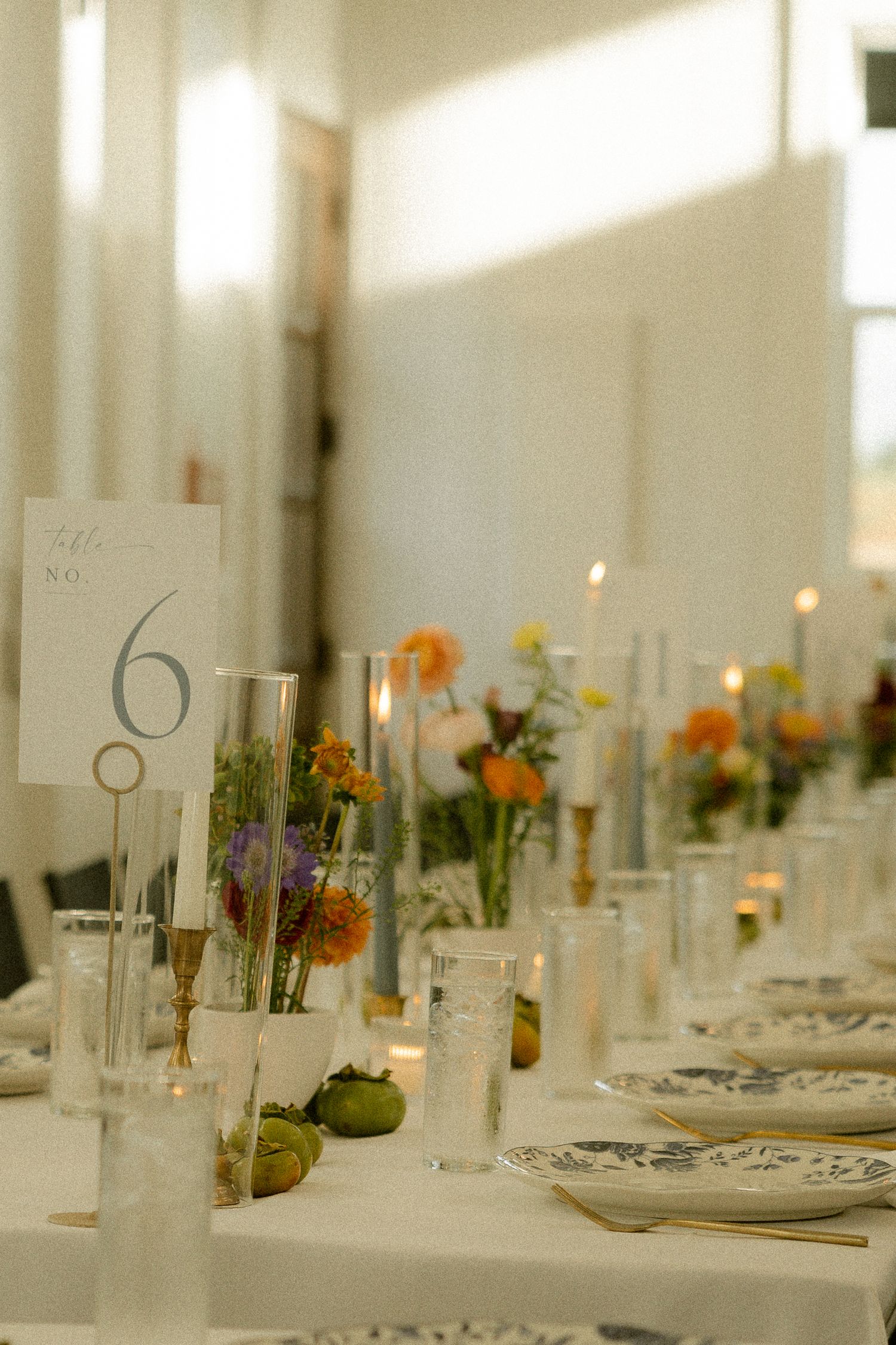 Elegant wedding reception table settings with orange floral centerpieces and table numbers.