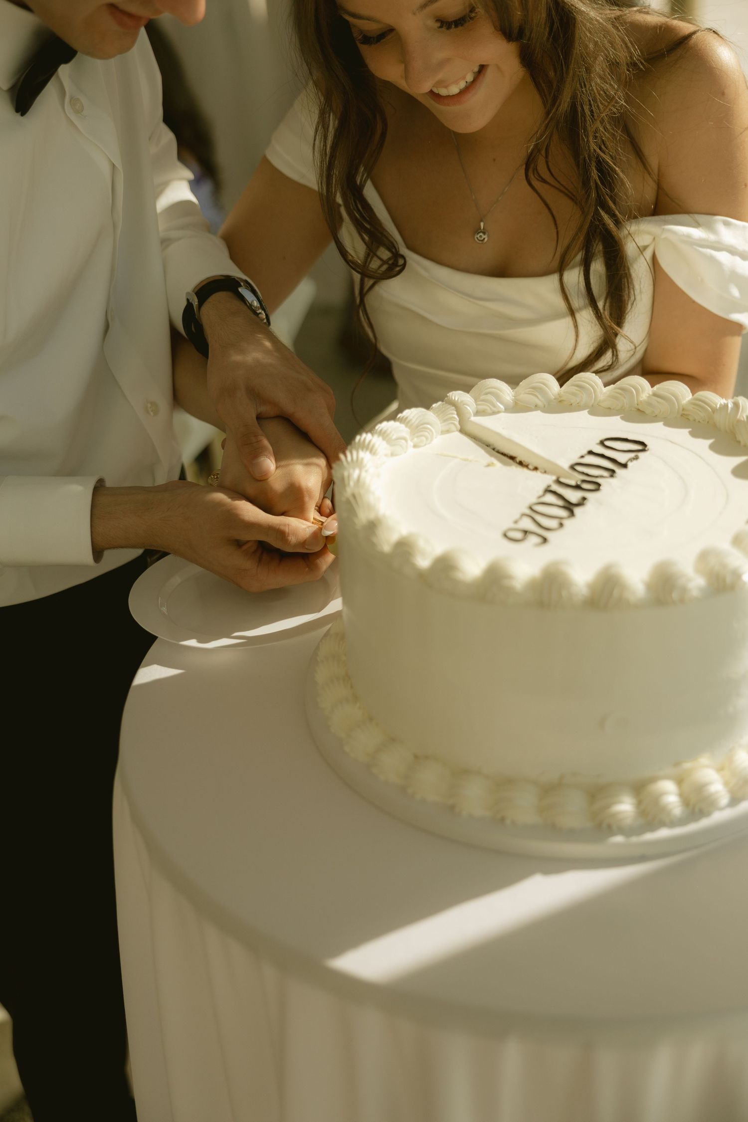 Bride and groom cutting their white wedding cake together, smiling joyfully.