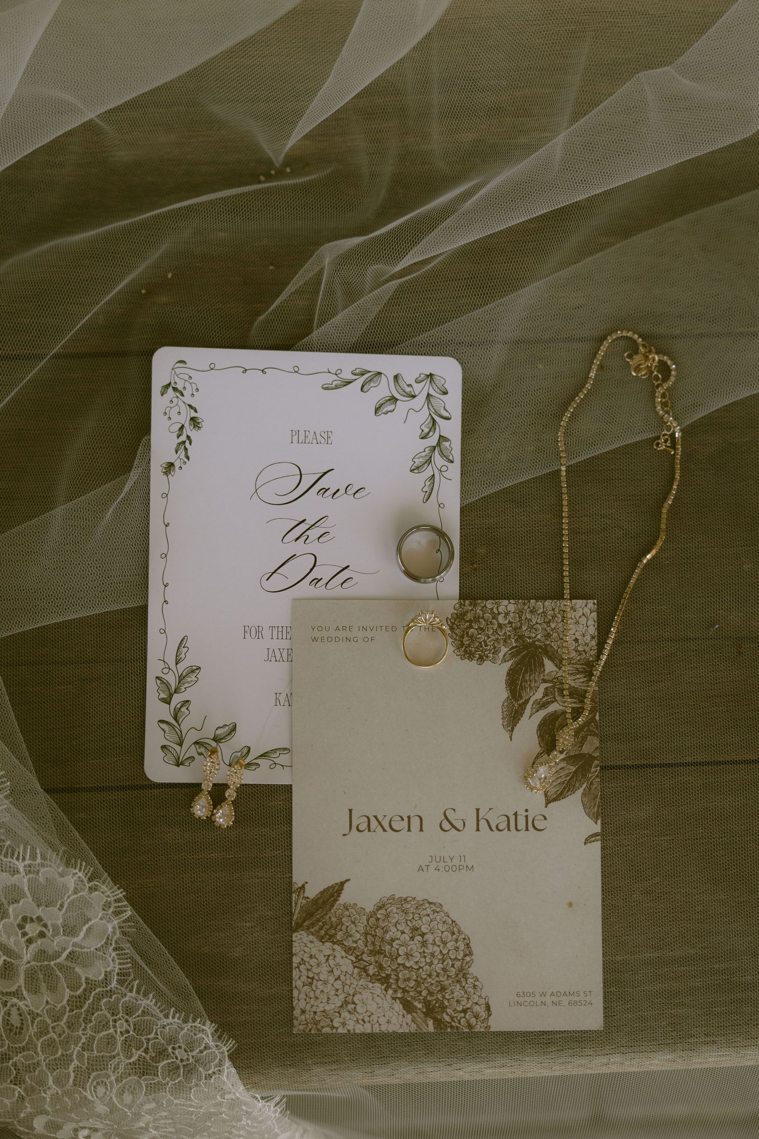 Elegant wedding save the date cards for Jaxen and Katie displayed with gold jewelry and lace veil on wooden surface.