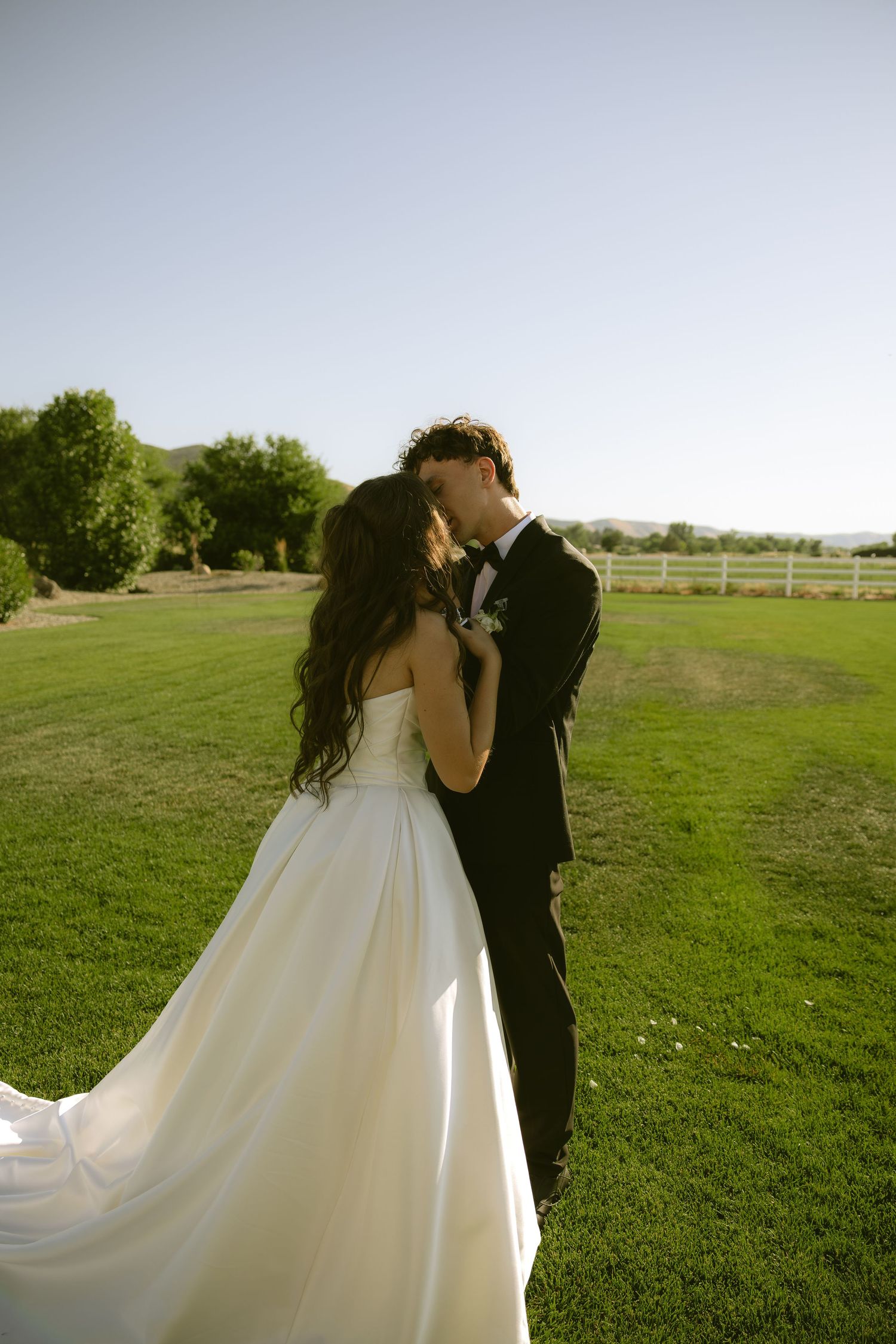 Bride and groom sharing romantic kiss on lush green grass at outdoor wedding.